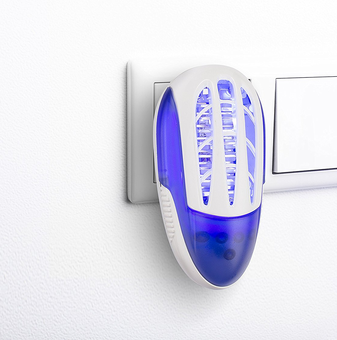 A white and blue insect killer plugged into a wall outlet on a white wall.