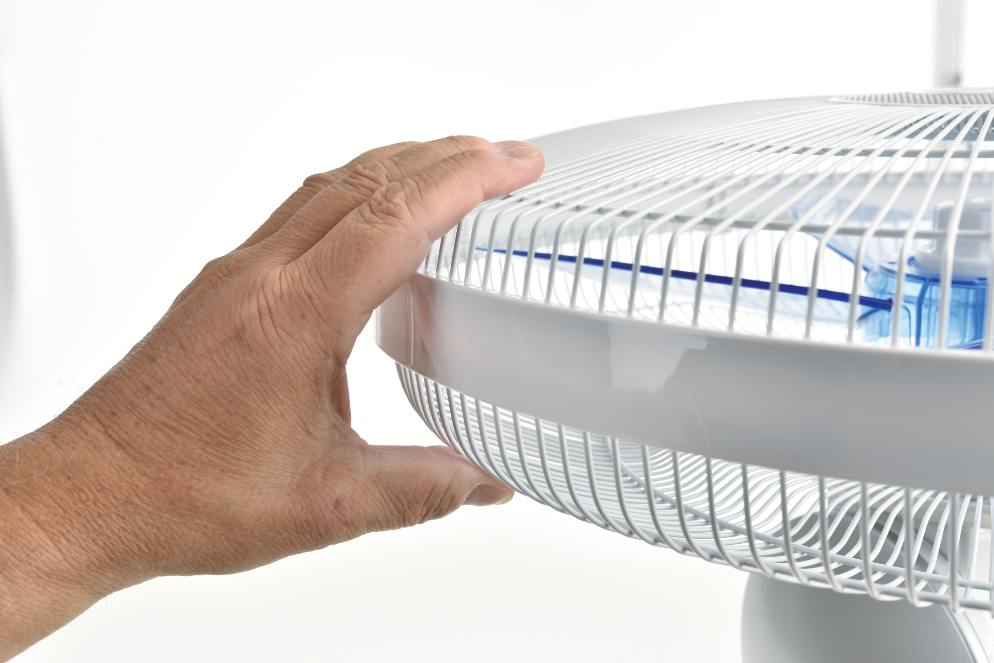 A hand touches a white electric fan. The fan has a protective grill and blue blades. The background is plain white.