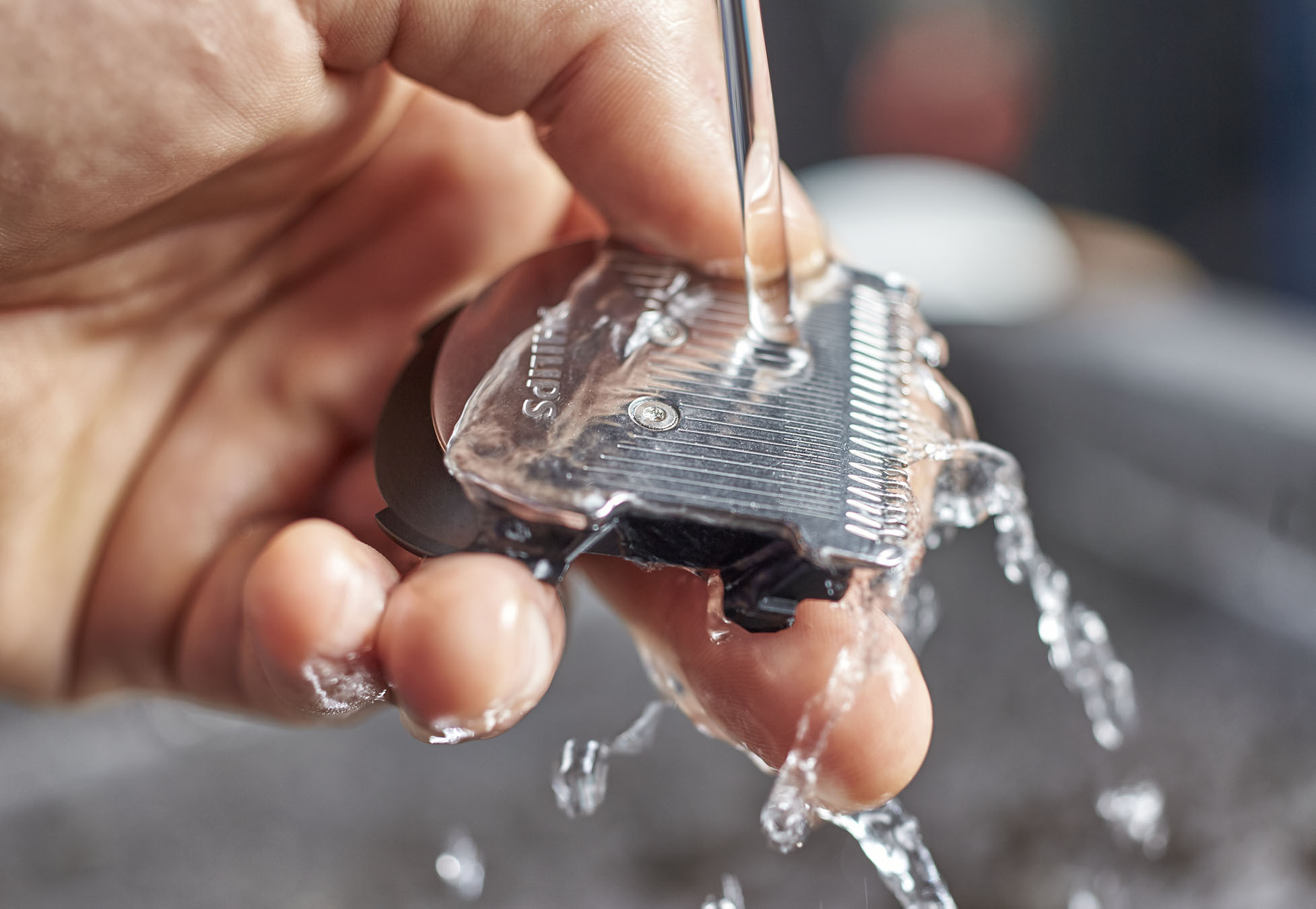 Hand, die einen Rasiererkopf hält, der mit Wasser gespült wird.