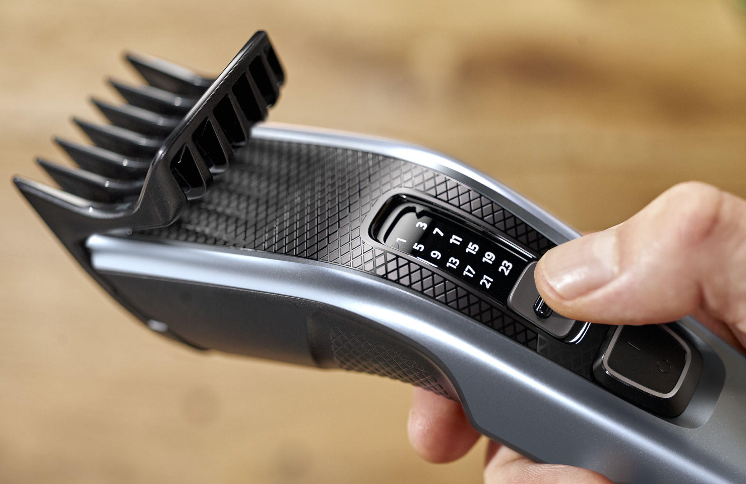 Eine Hand, die die Längeneinstellung eines Haarschneiders anpasst, mit sichtbarer Skala und schwarzem Kamm.