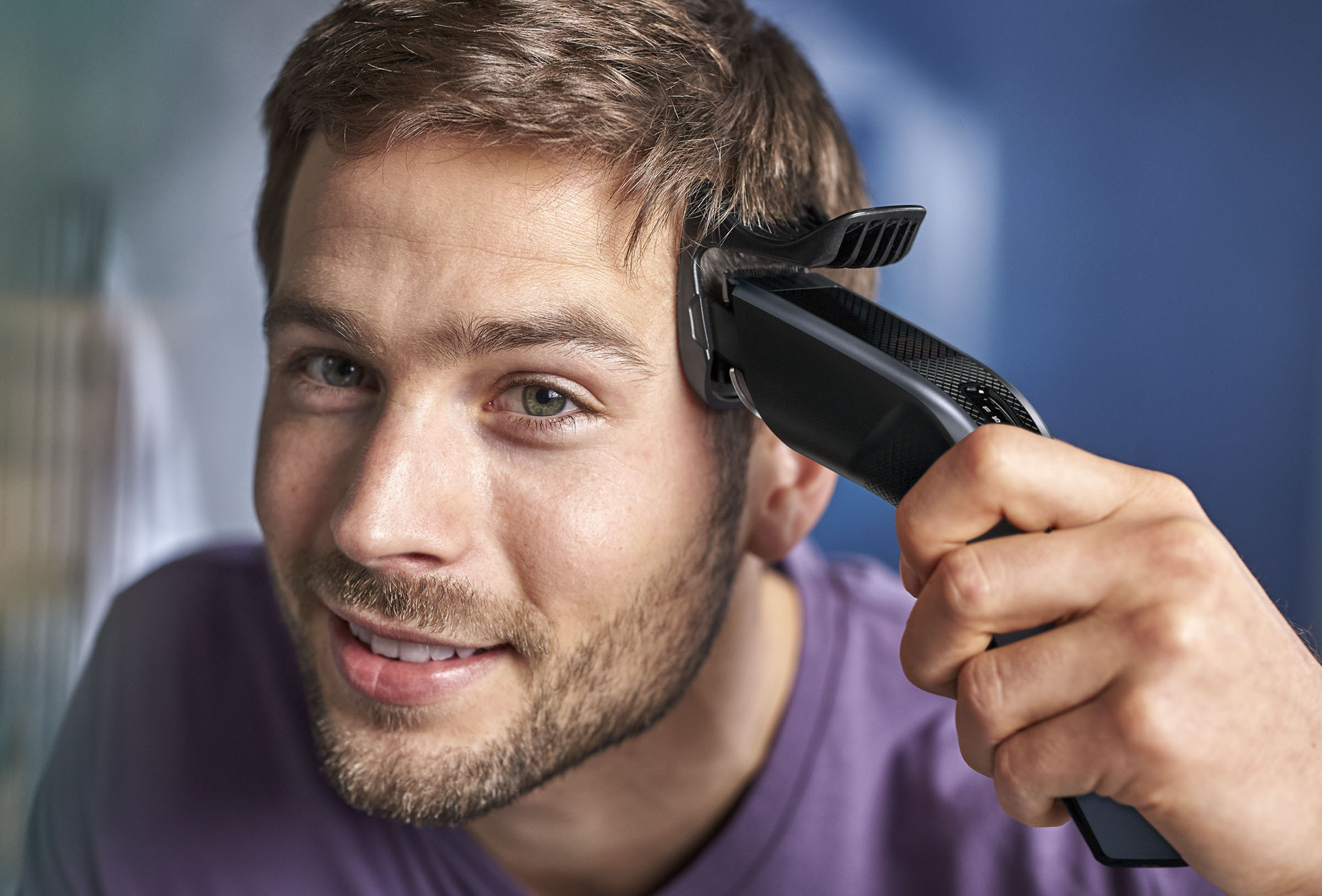 Mann rasiert sich mit einem Philips Haarschneider die Haare auf dem Kopf. Er lächelt.