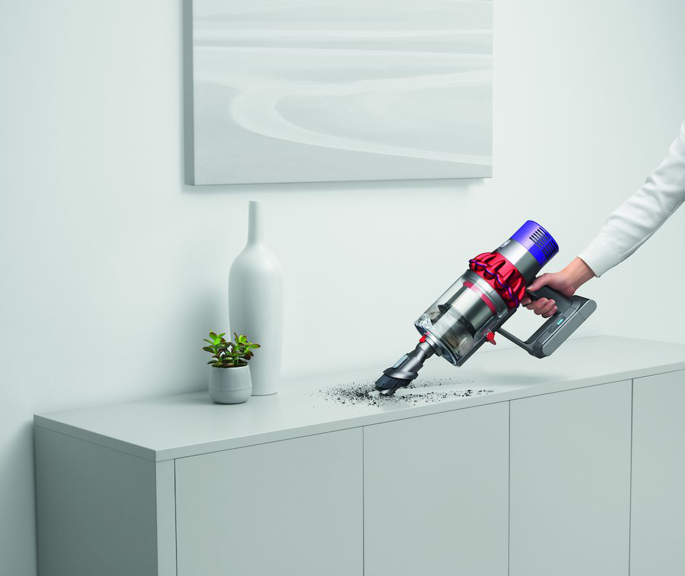 Een persoon stofzuigt een wit oppervlak met een Dyson stofzuiger.