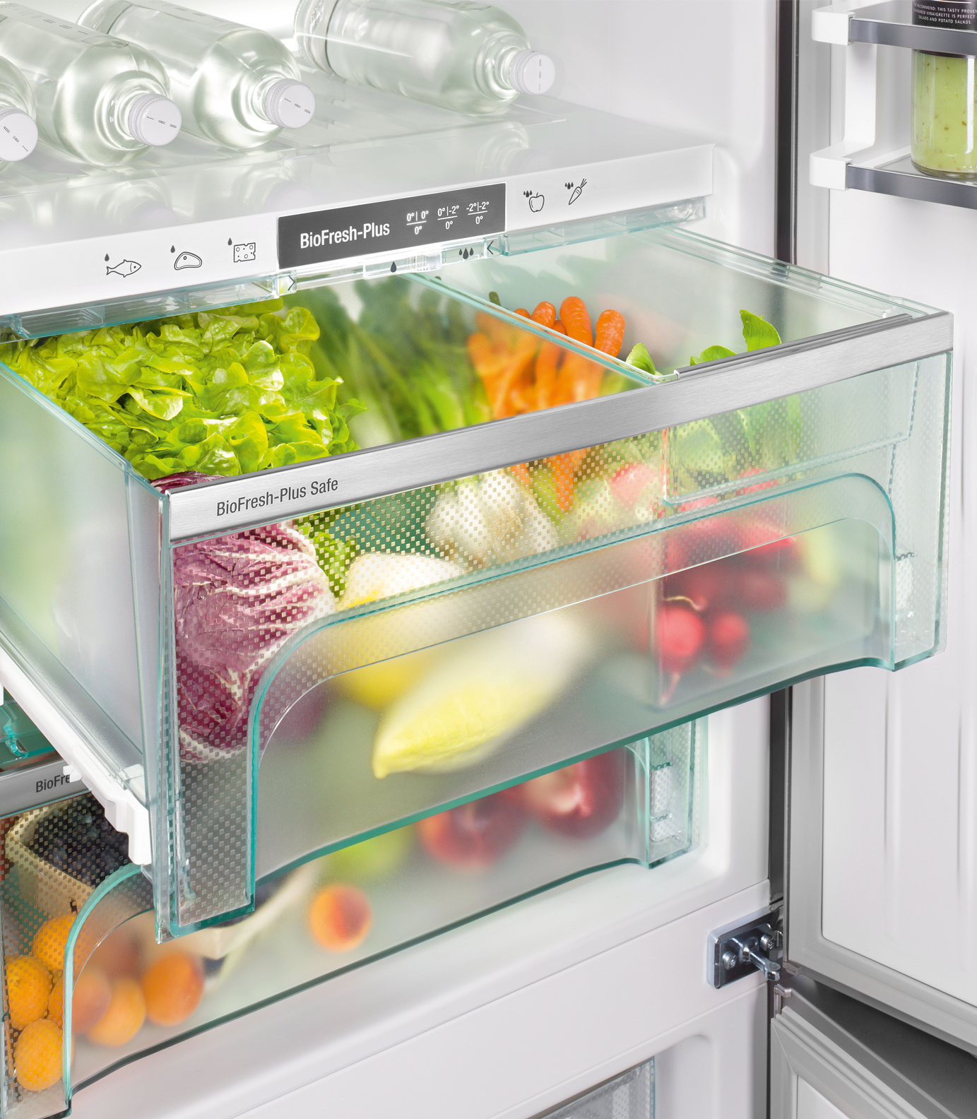 Open fridge with produce. Contains lettuce, carrots, radishes, and other vegetables. Water bottles are in the top shelf.