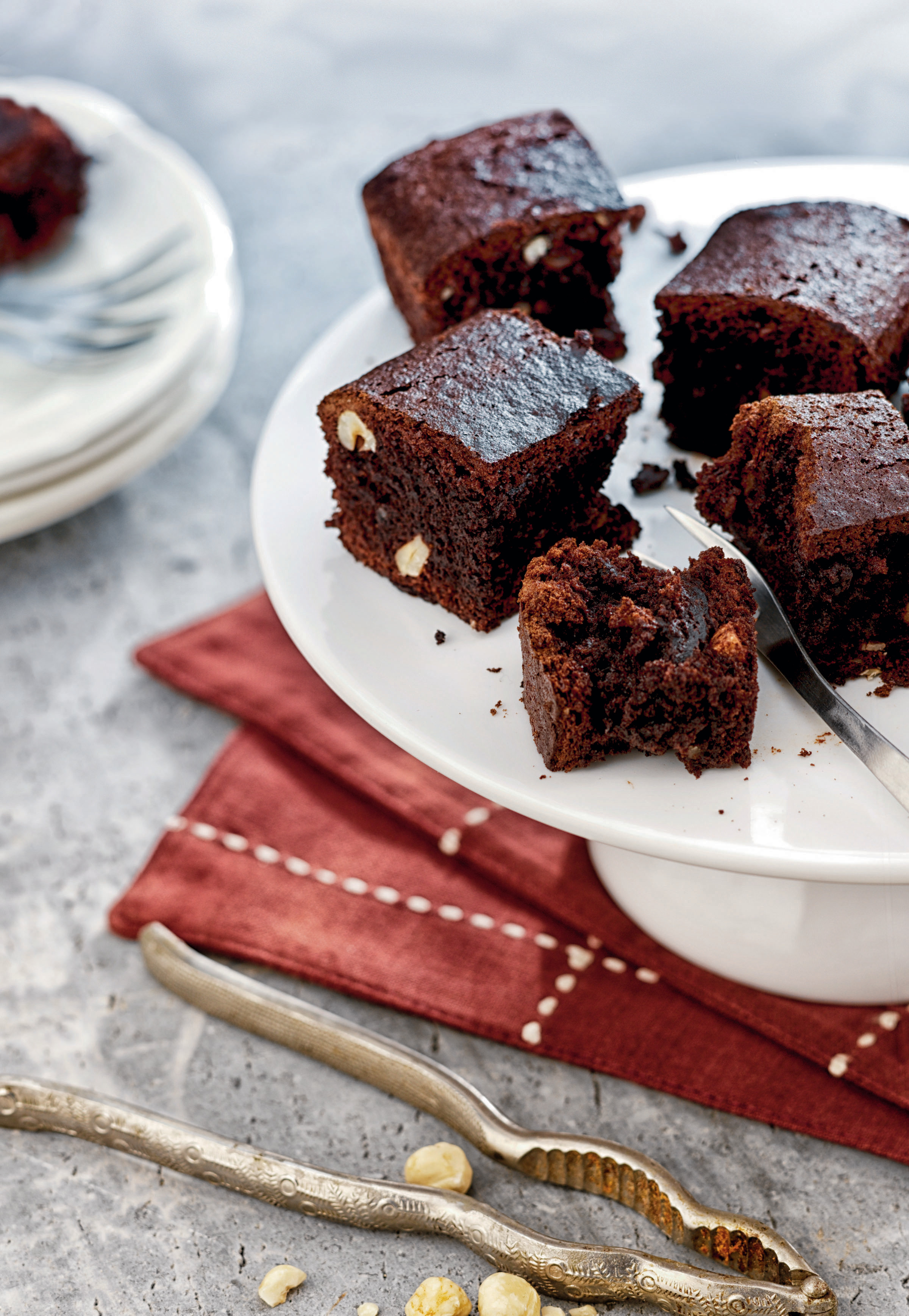 Brownie-Quadrate auf einem weißen Sockel. Eine Gabel ist in einem. Nussknacker und Nüsse sind im Vordergrund.
