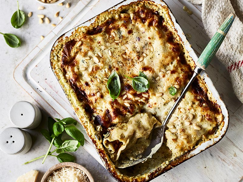 Gebackene Lasagne in einer weißen Schüssel. Sie hat eine Käse- und Basilikum-Schicht.