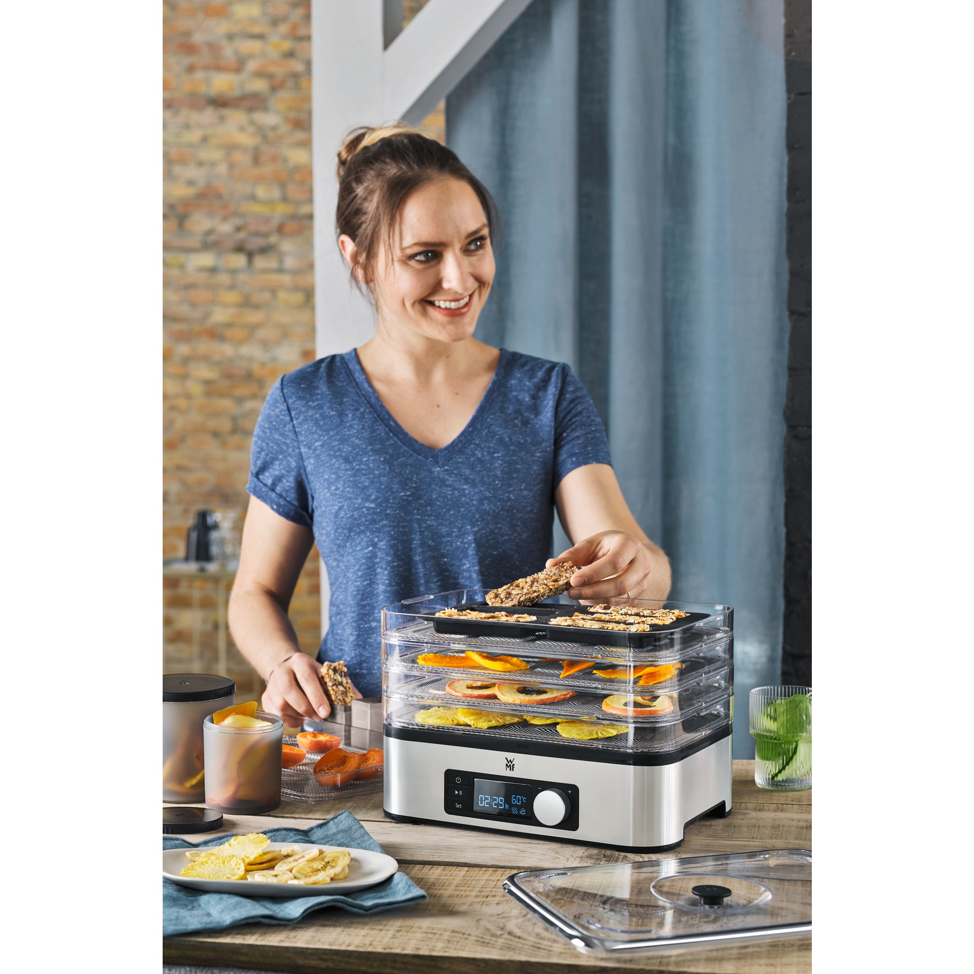 Vrouw met een voedseldroger. Ze houdt een snack vast, en de machine heeft trays.