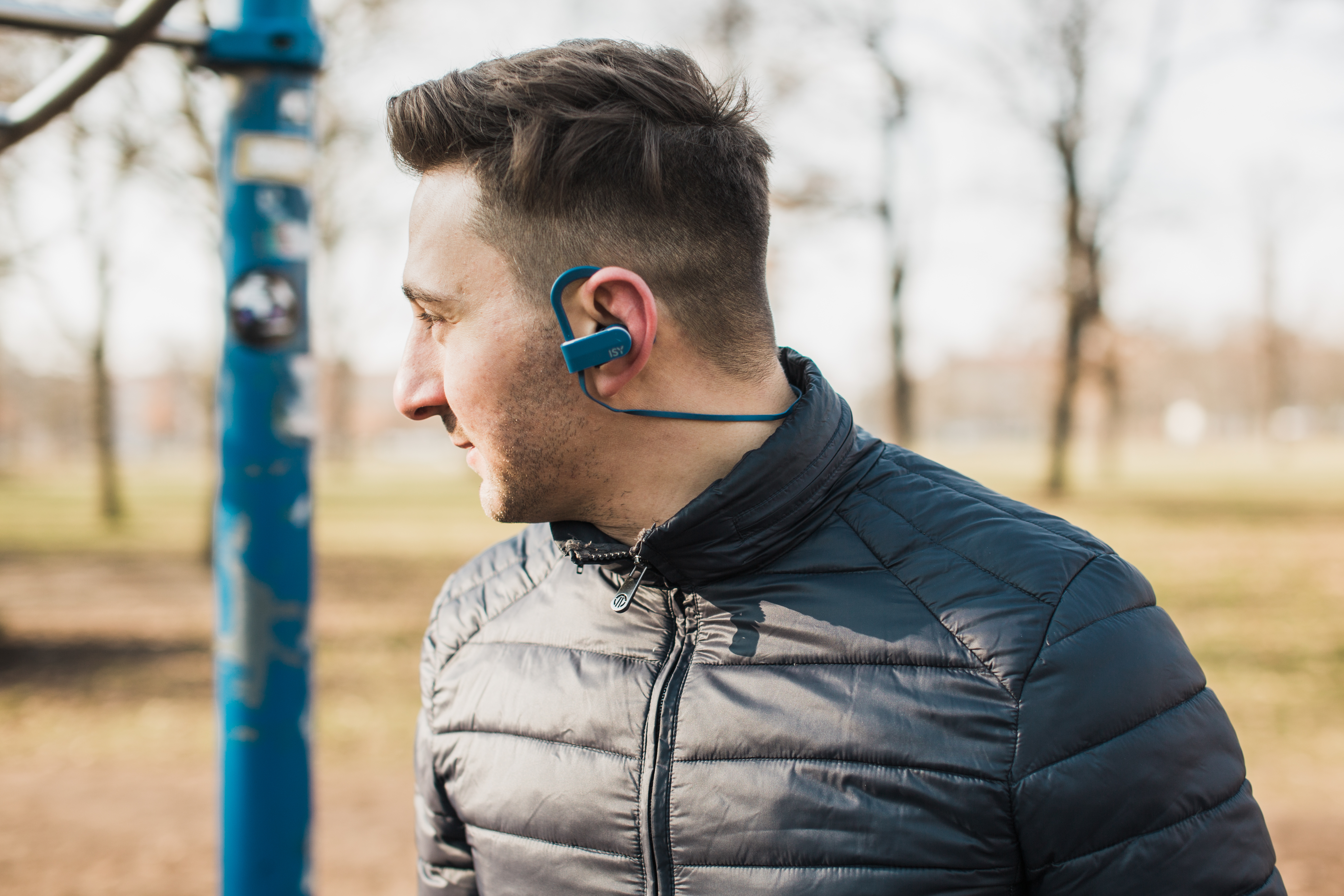 Mann mit Kopfhörern, der wegschaut. Ein Park mit Bäumen im Hintergrund.