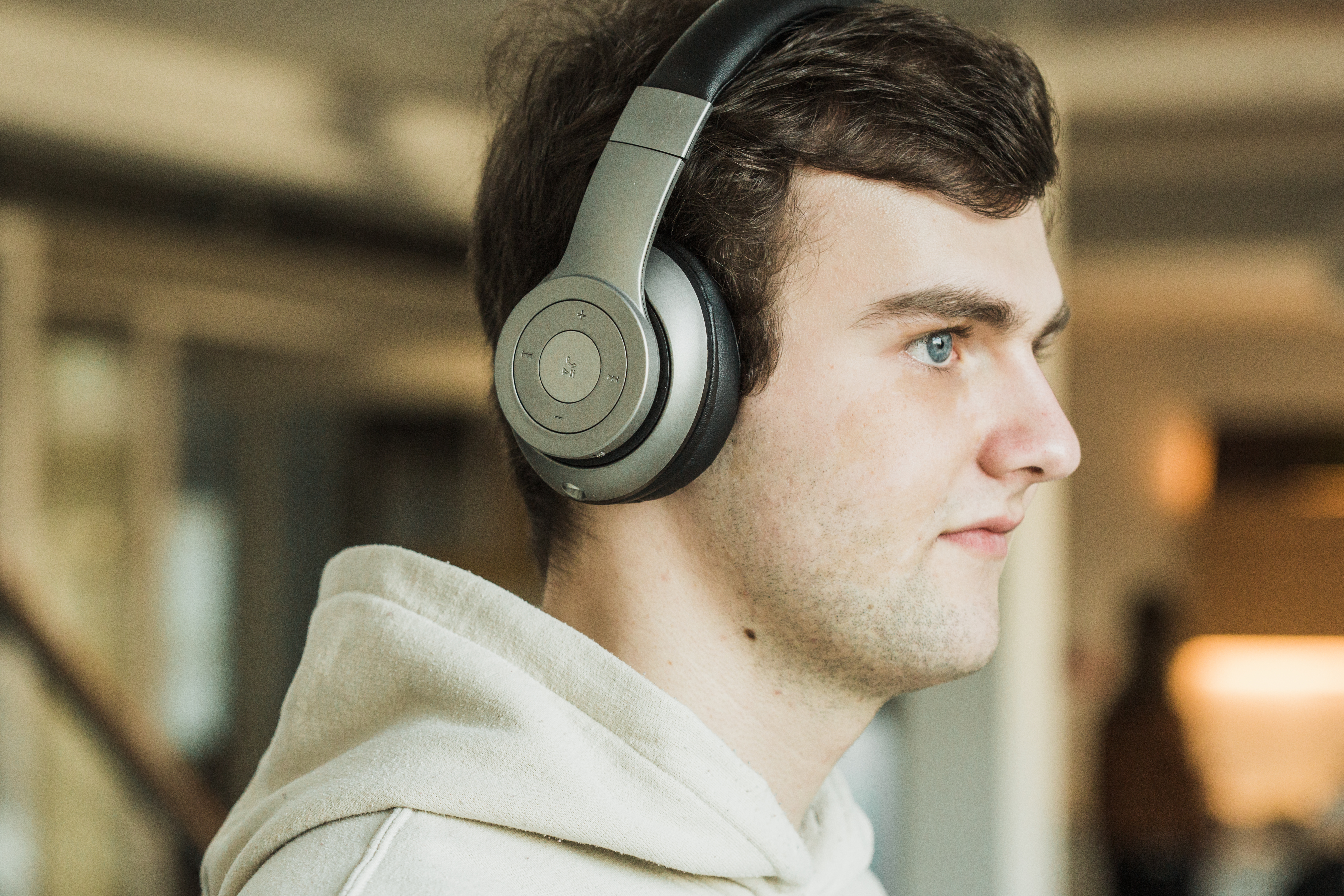 Ein junger Mann mit grauen Kopfhörern, der nach rechts schaut. Er trägt einen hellen Kapuzenpullover.