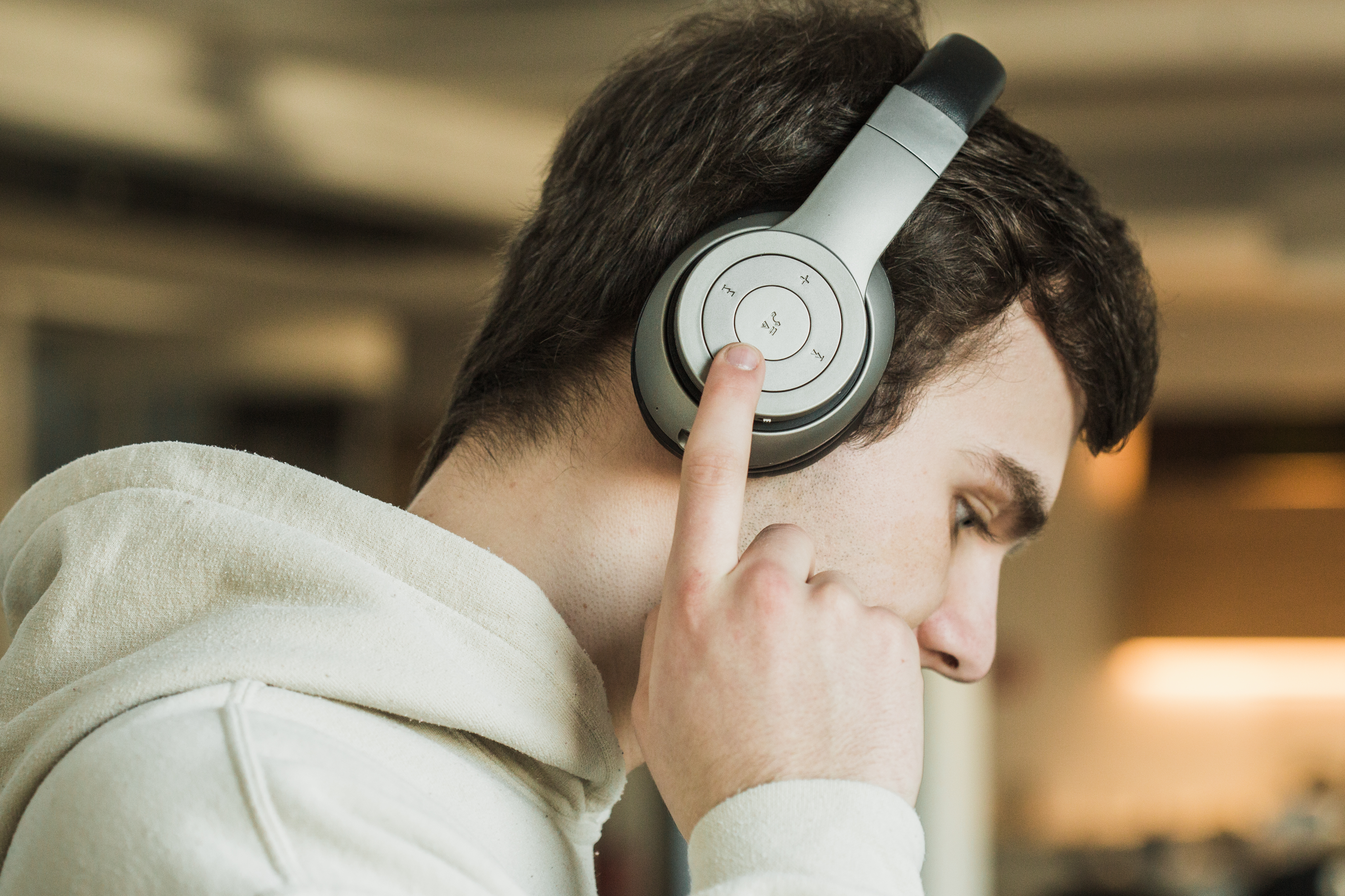 Mann mit silbernen Kopfhörern, berührt einen Knopf an der rechten Ohrmuschel.