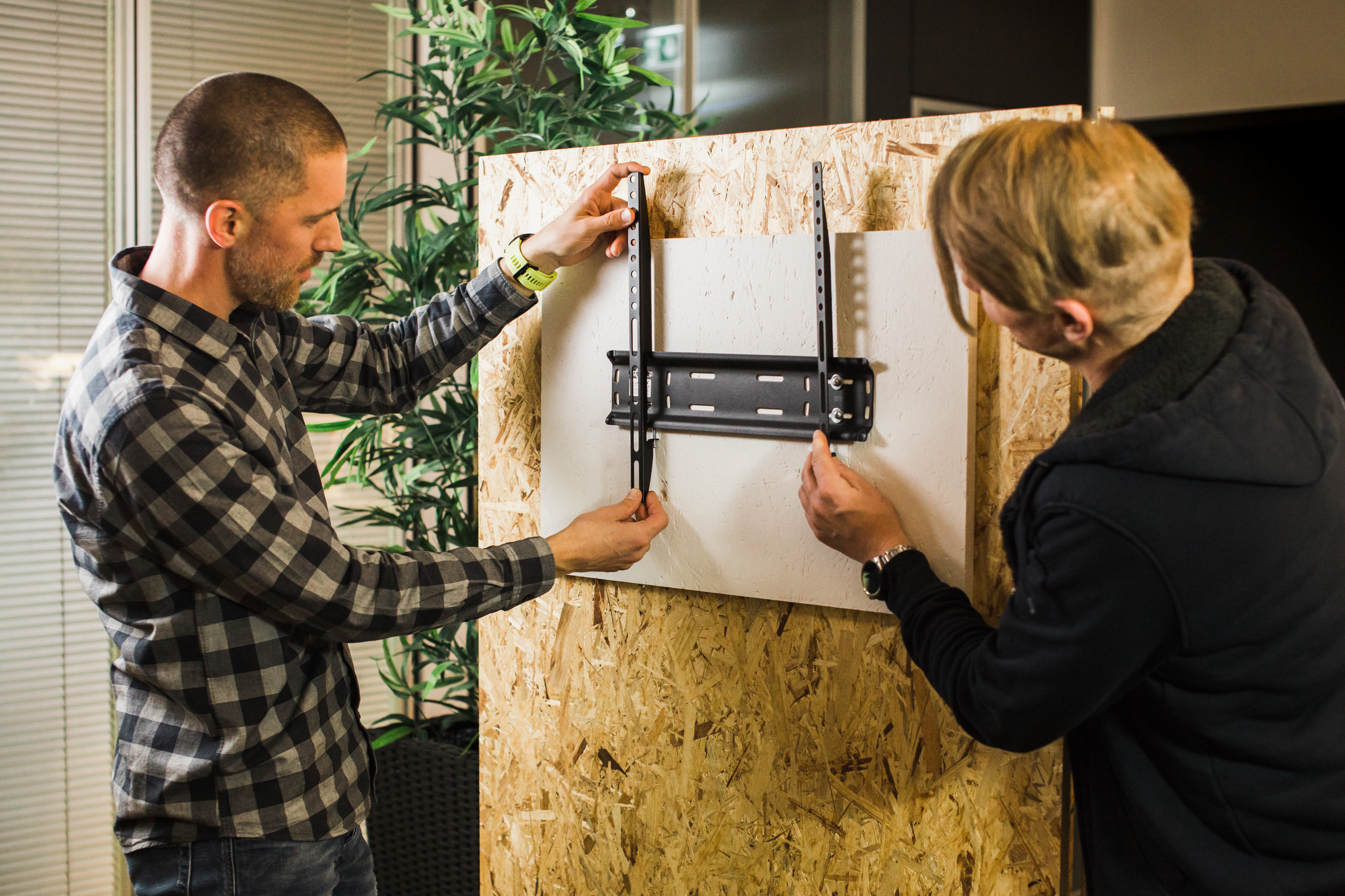 Zwei Männer arbeiten an einer Wandhalterung für einen Fernseher.