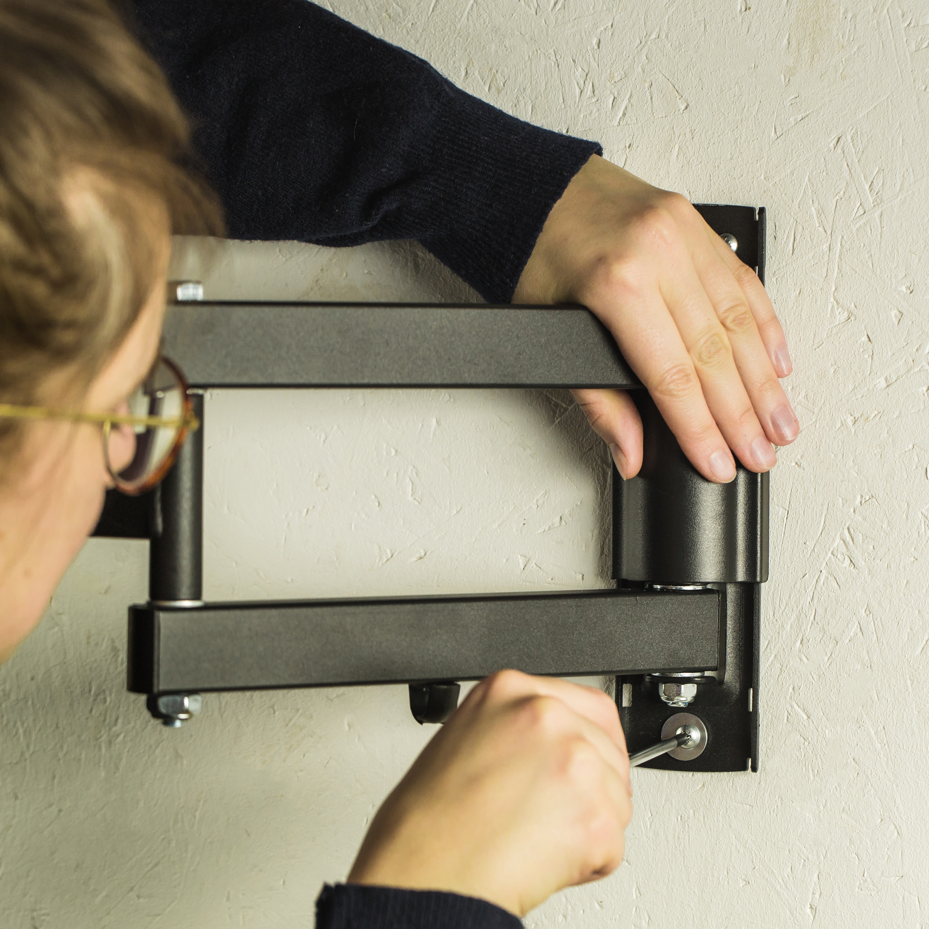 Una persona che installa un supporto a parete per TV nero su una parete strutturata bianco sporco.