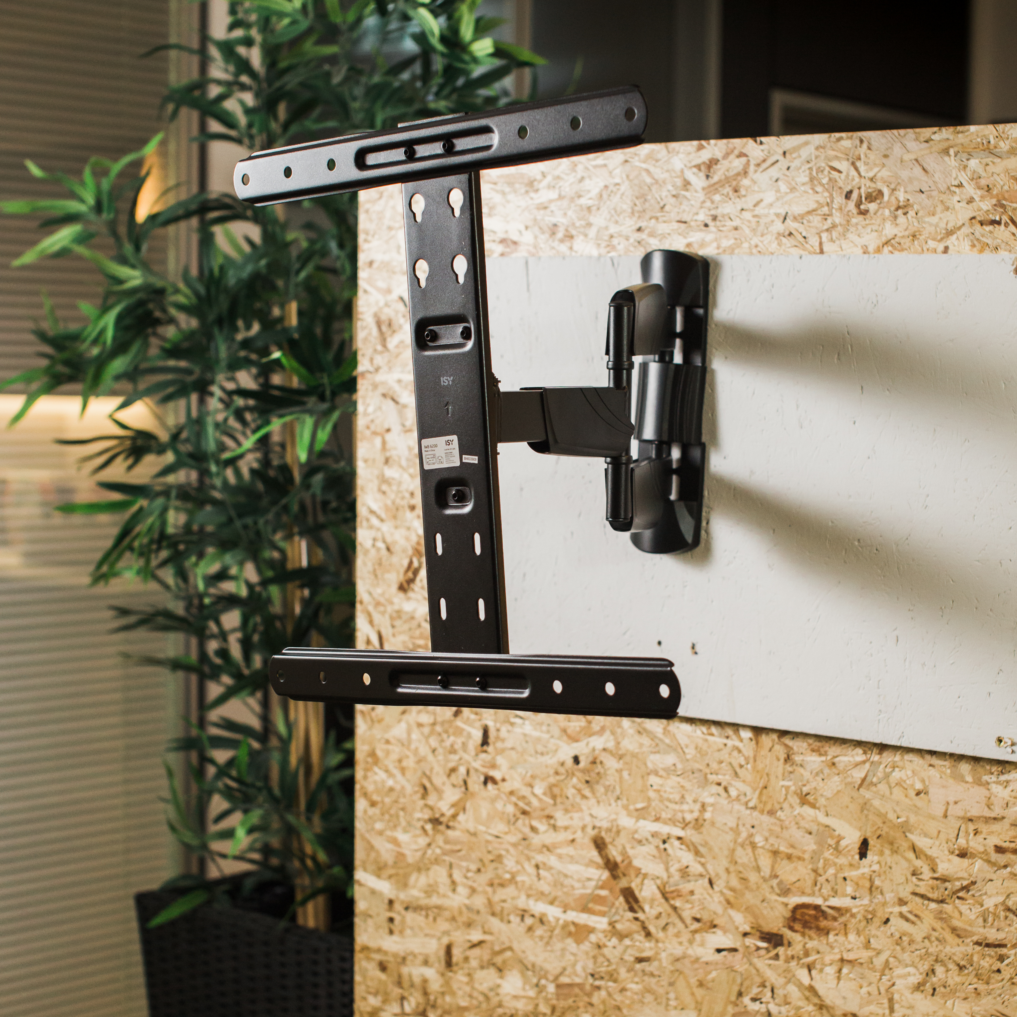 Un support de télévision noir installé sur un mur en bois, avec une plante verte visible en arrière-plan.