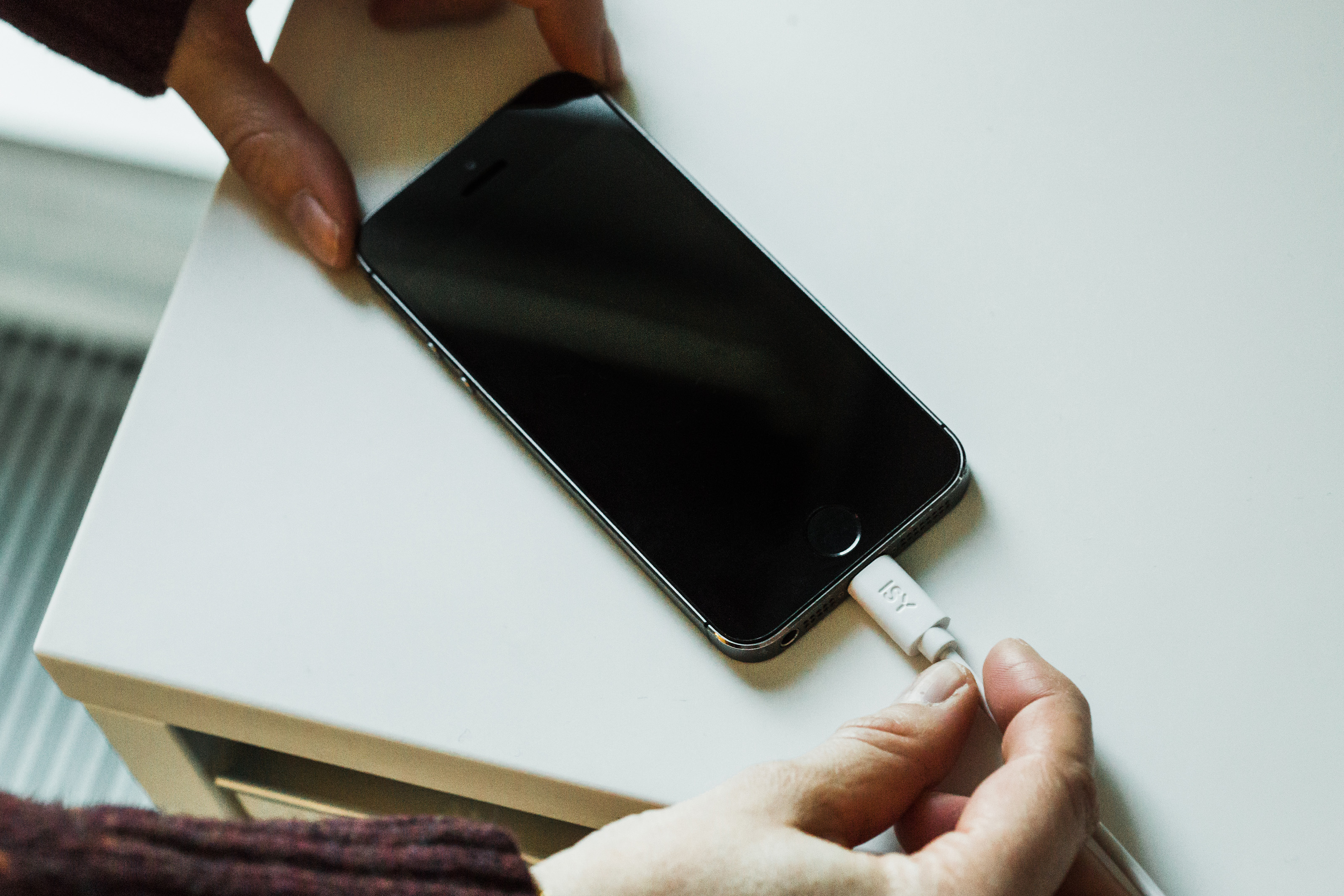 Mains branchant un chargeur blanc sur un smartphone noir sur une table blanche.