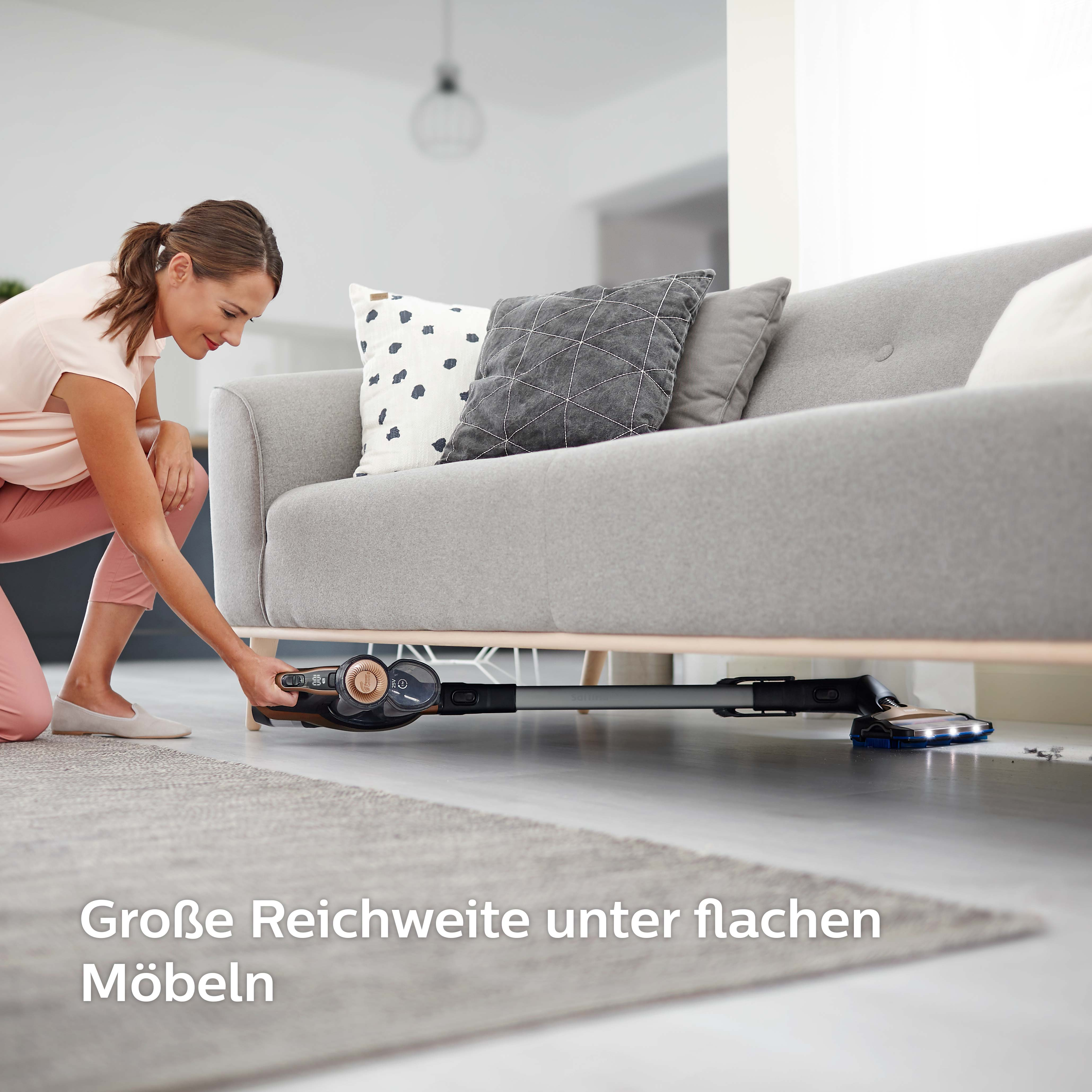 Eine Frau saugt mit einem Staubsauger unter einem Sofa. Text ist sichtbar.