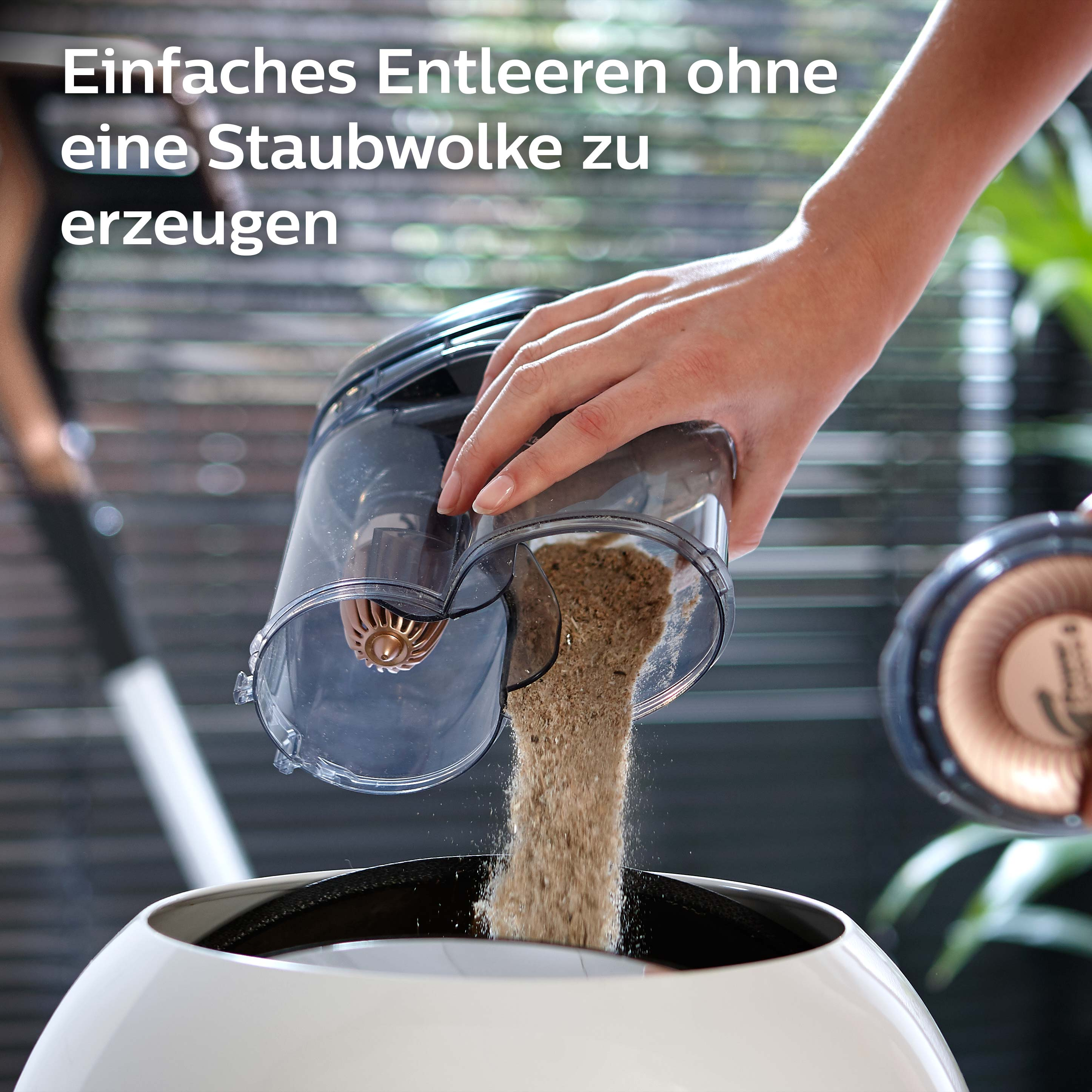 Eine Person entleert einen Staubbehälter eines Staubsaugers. Brauner Staub fällt in einen weißen Behälter.