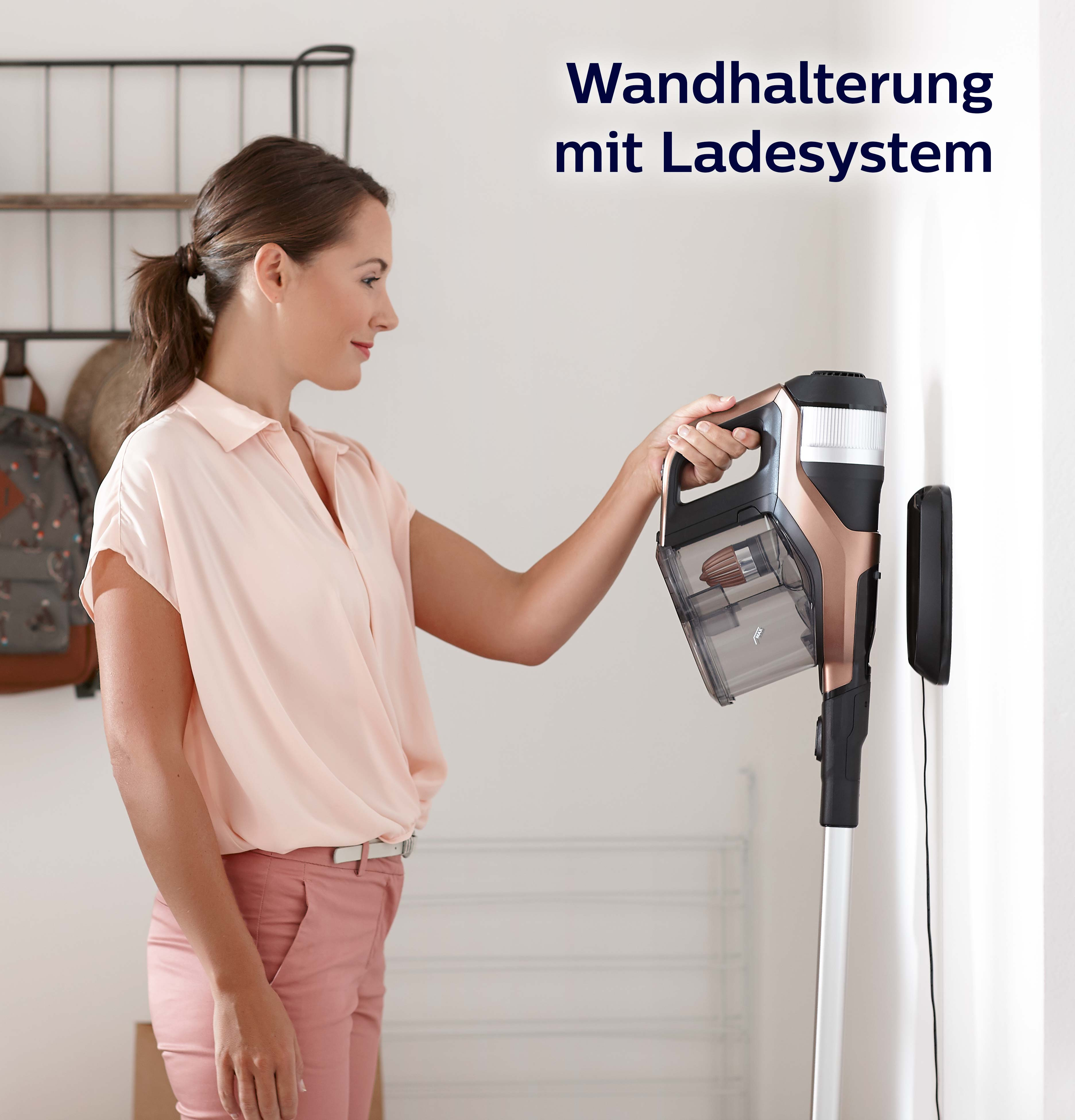 Frau benutzt einen kabellosen Staubsauger. Wandhalterung mit Ladesystem sichtbar.