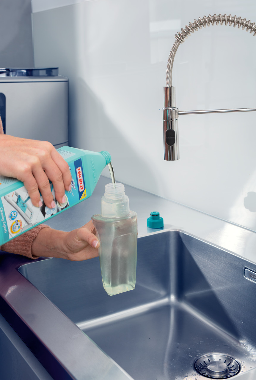 Eine Person gießt Reinigungsflüssigkeit in eine Spenderflasche über einem Edelstahlbecken.
