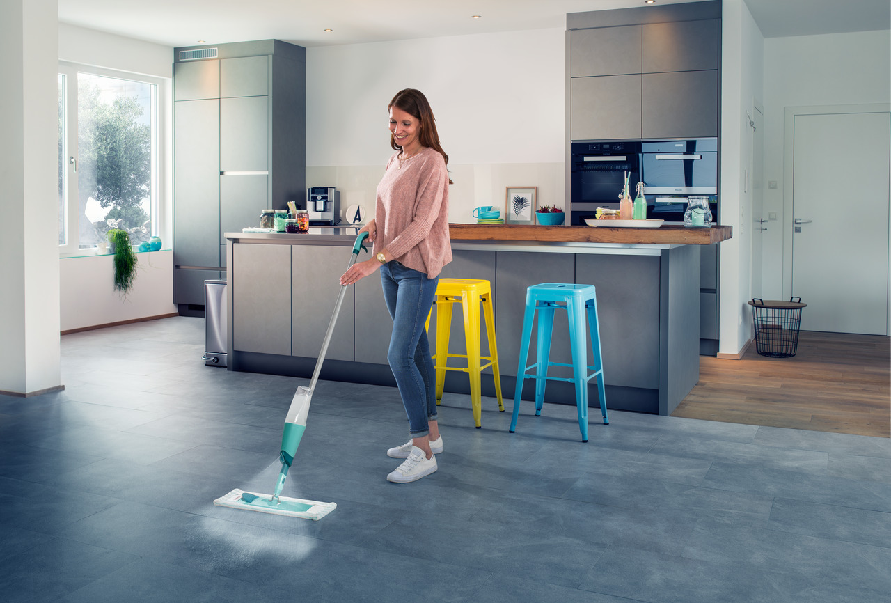 Frau wischt Küchenboden. Ein paar Hocker sind hinter ihr.