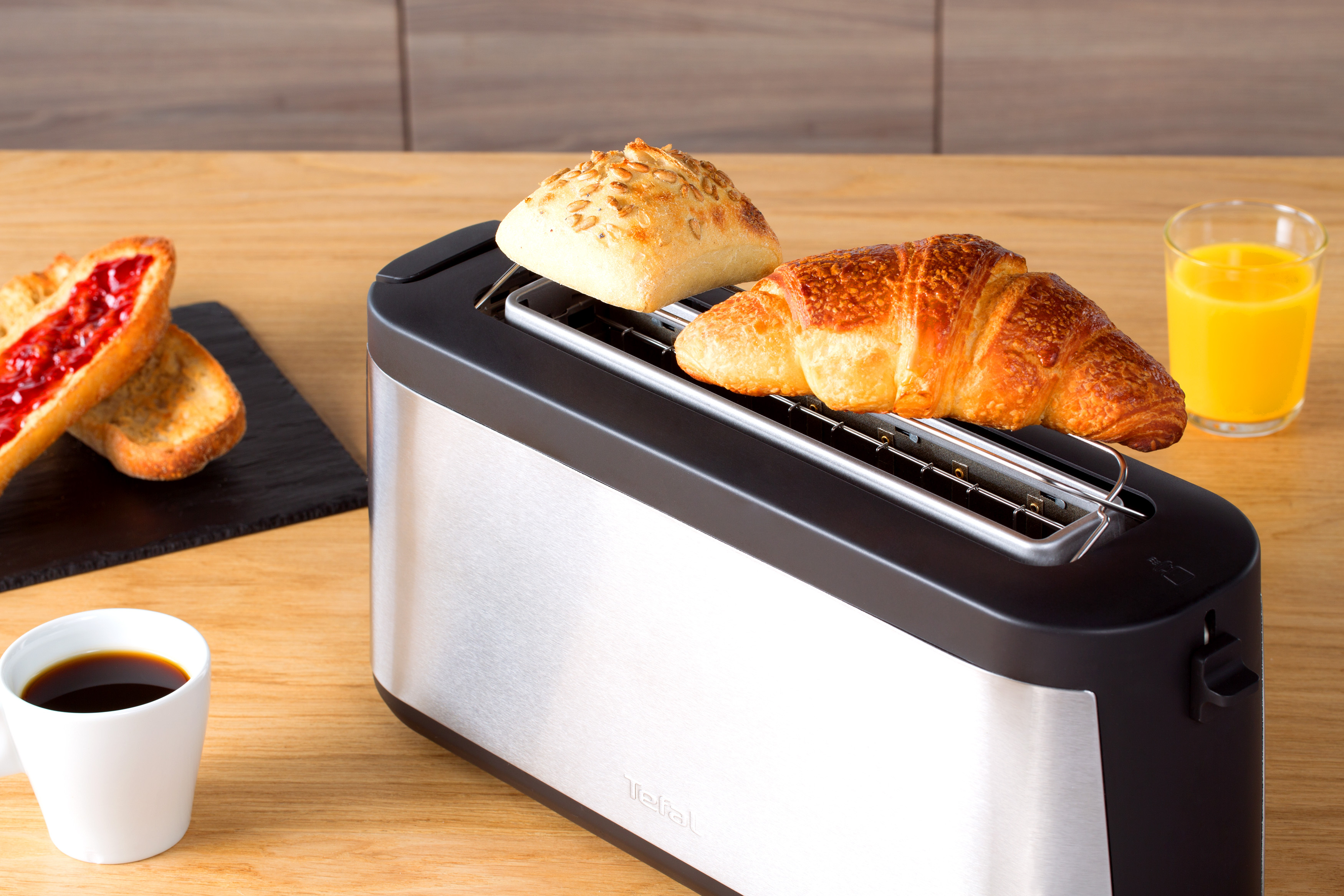 Toaster mit Brot, Croissant und einem Glas Saft auf einem Holztisch.