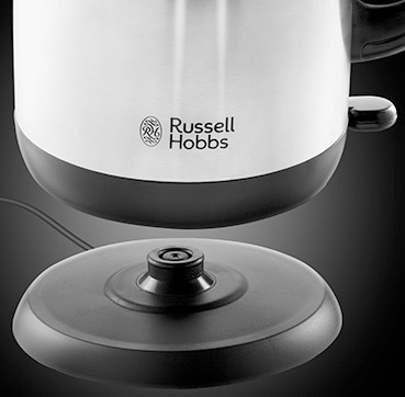 A stainless steel electric kettle with a black base and a black stand on a dark background.