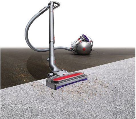 Ein Staubsauger reinigt einen Teppich. Die Maschine ist silber und rot.