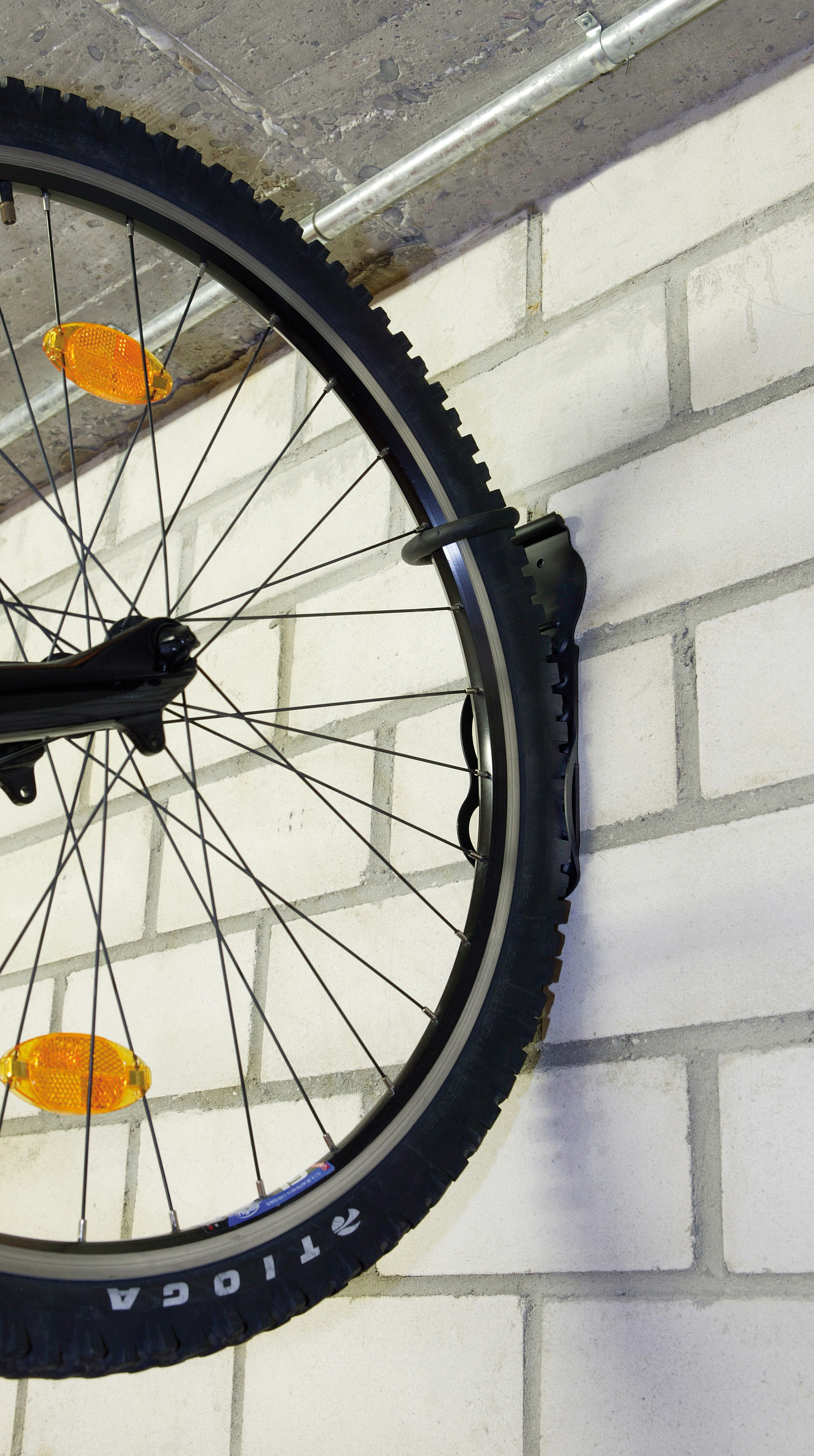 Fahrradrad an einer weißen Ziegelmauer montiert. Rad ist schwarz mit orangenen Reflektoren.