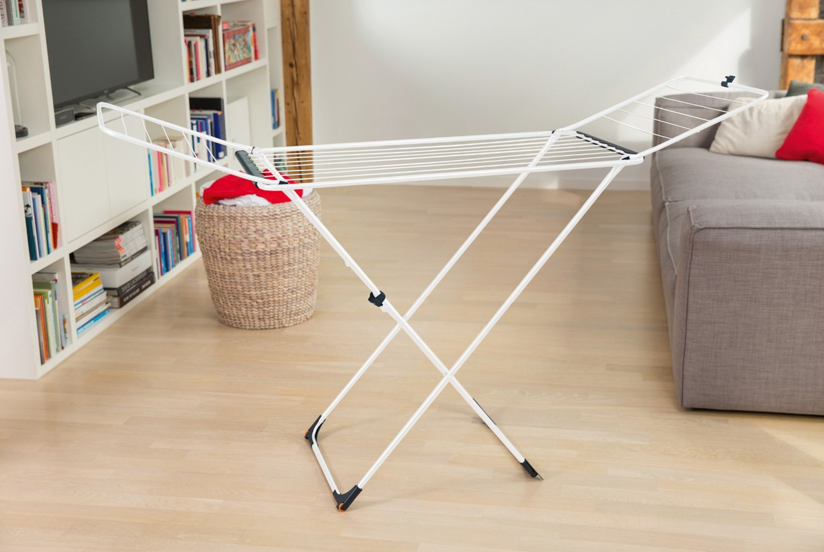 Weißer Wäscheständer, teilweise geöffnet, in einem Raum mit Holzboden und Sofa.