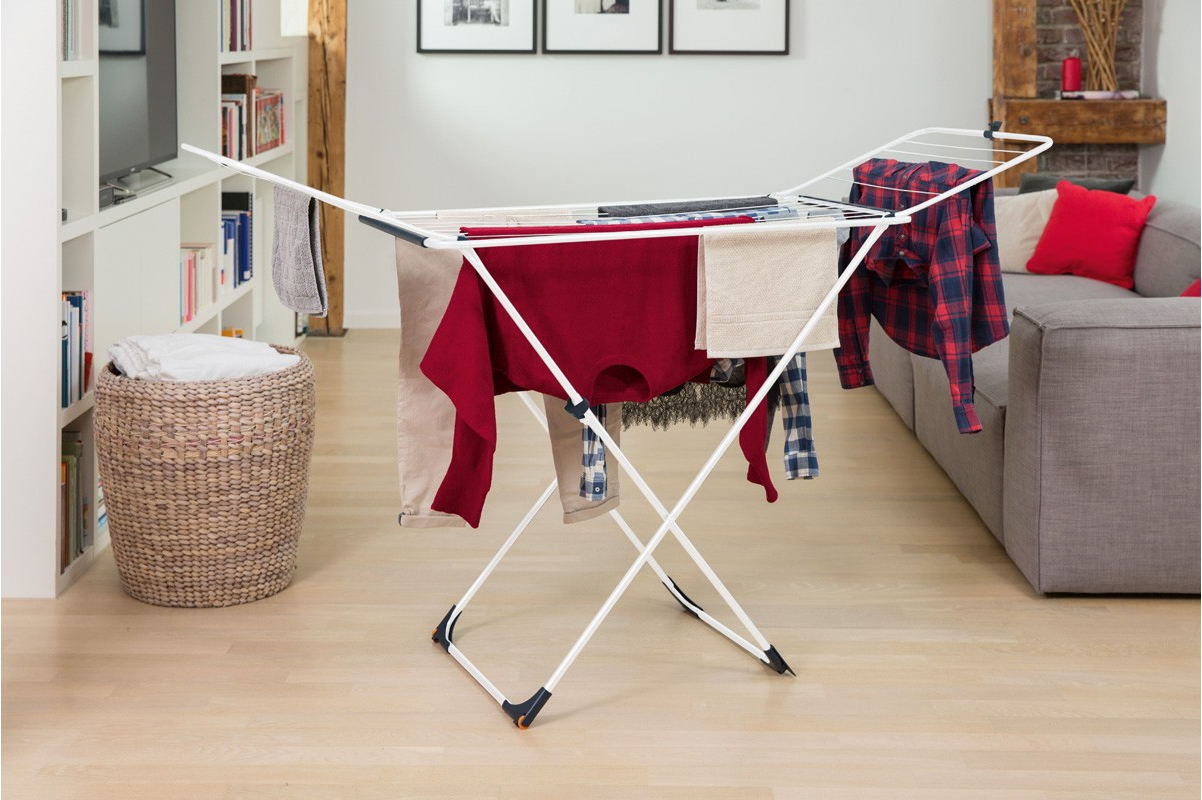Weißer Wäscheständer mit Kleidung, die daran hängt, in einem Raum mit Sofa und Fenster.