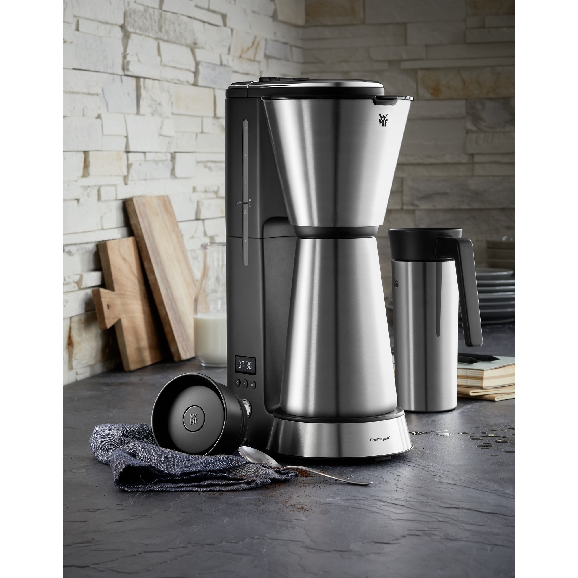 Rvs koffiezetapparaat met een kan, een thermosbeker en een lepel op een aanrecht.
