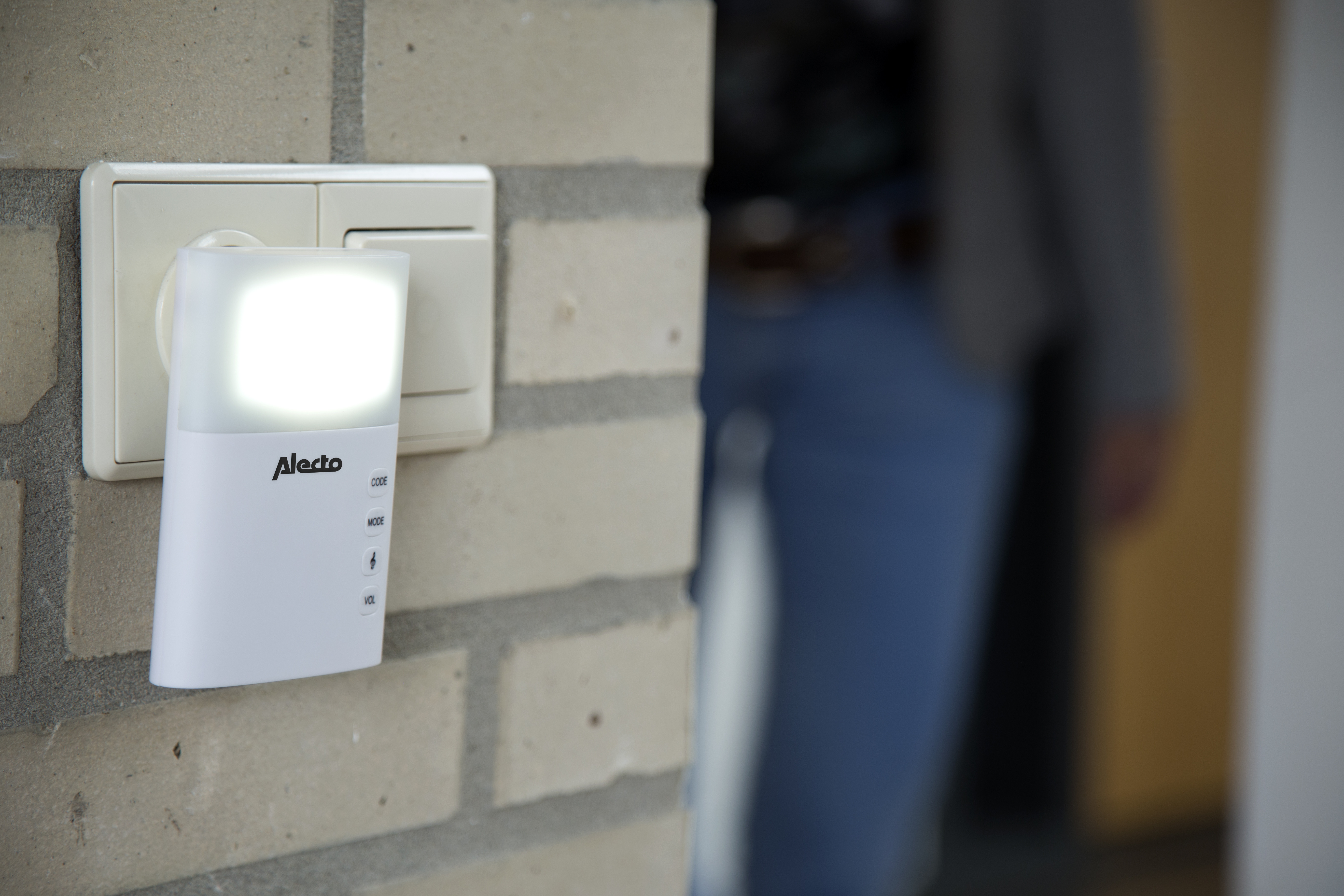 White night light plugged into a wall outlet. A person is in the background, slightly out of focus.