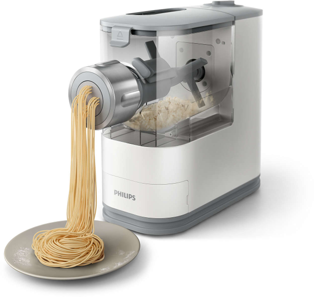 Fehér és szürke tésztakészítő gép, mely spagettit extrudál egy szürke tányérra. A tészta látható.