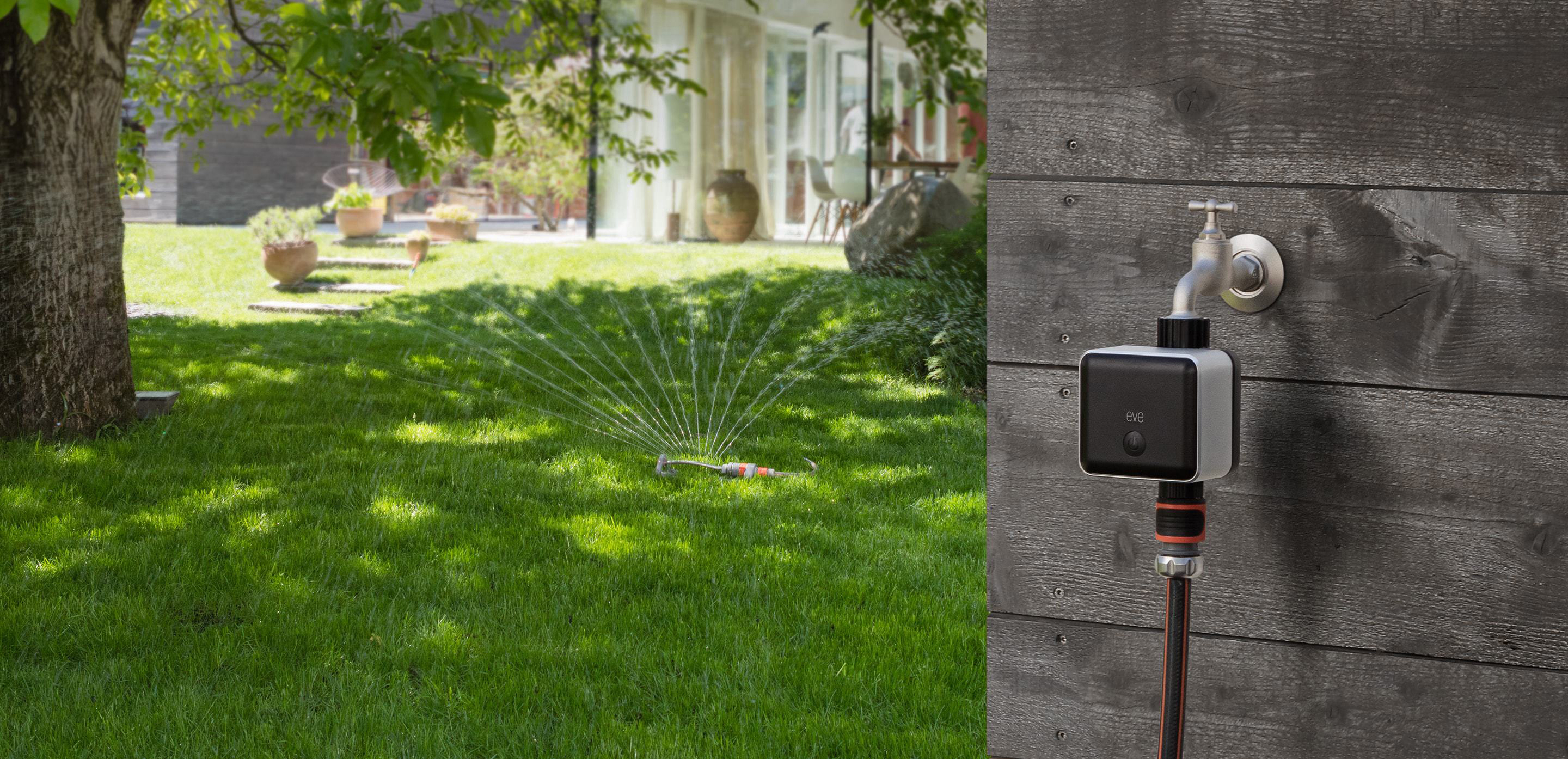 Rasen mit laufender Sprinkleranlage, Haus und Bäume im Hintergrund.