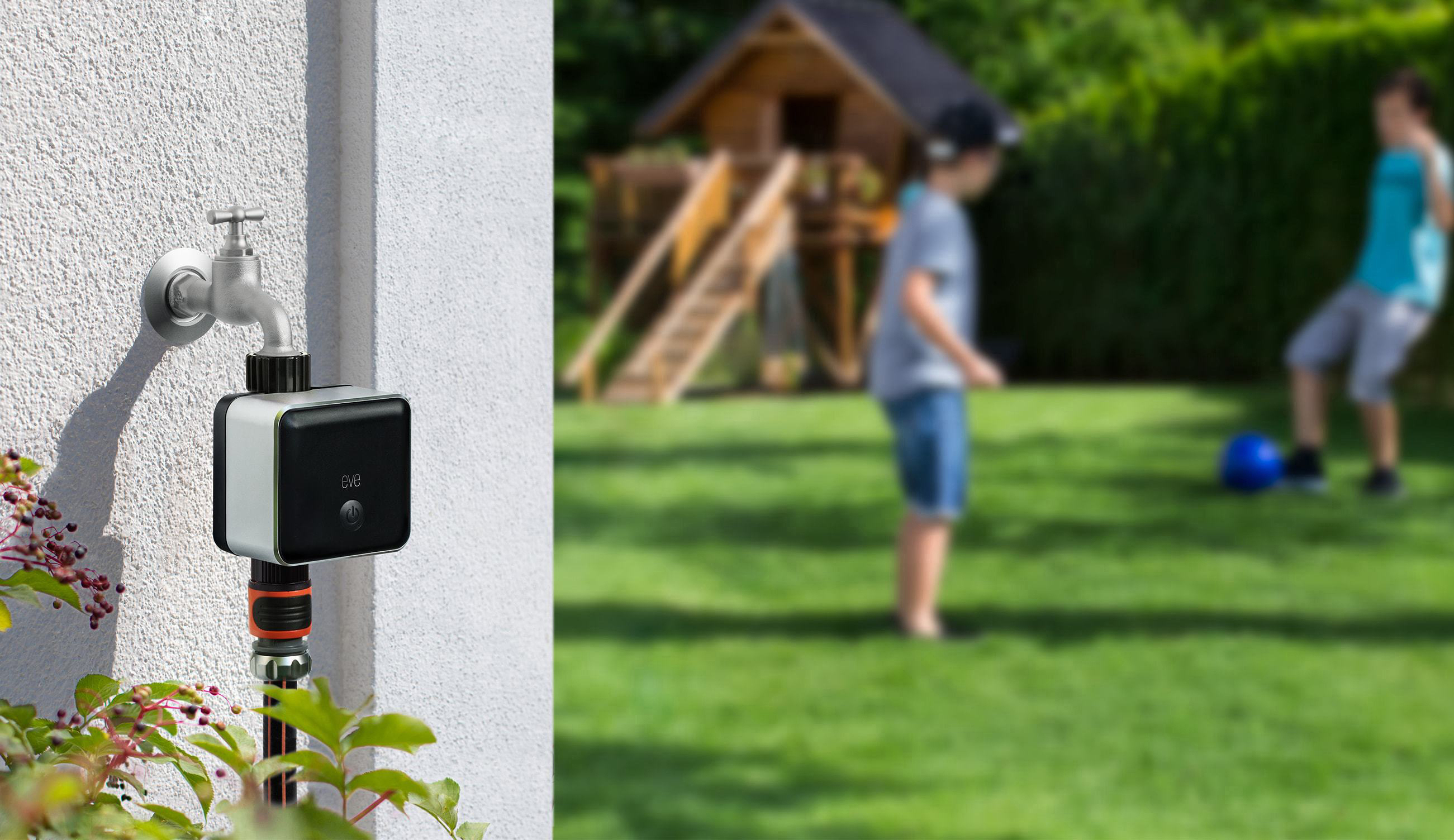 Ein wandmontierter Wasserhahn mit einem schwarzen Smart-Gerät und zwei Jungen, die im Hintergrund mit einem Ball spielen.