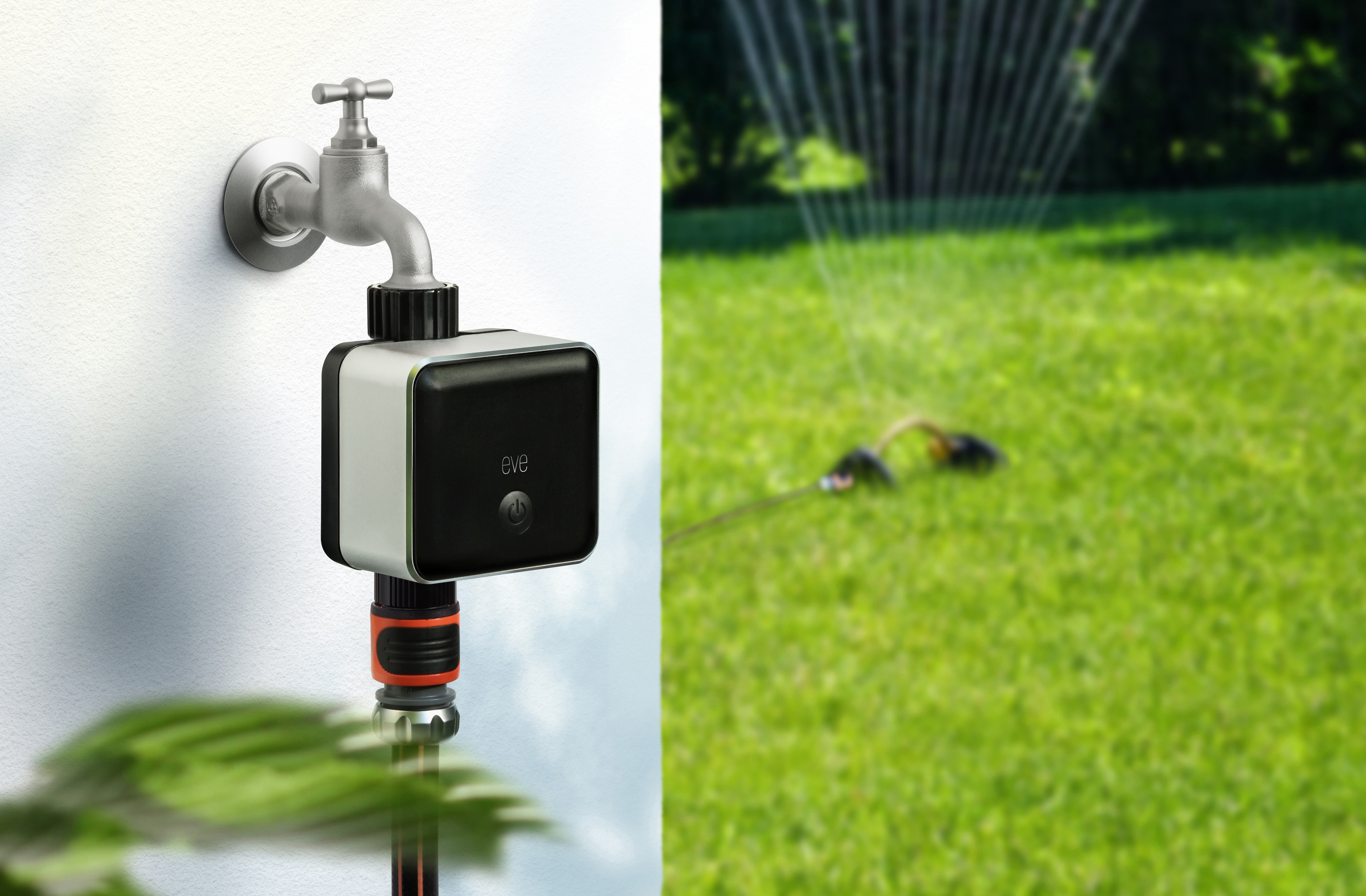 Ein Smart-Home-Wasserventil, das an einen Wasserhahn angeschlossen ist, Wasser sprüht auf einem grünen Rasen im Hintergrund.