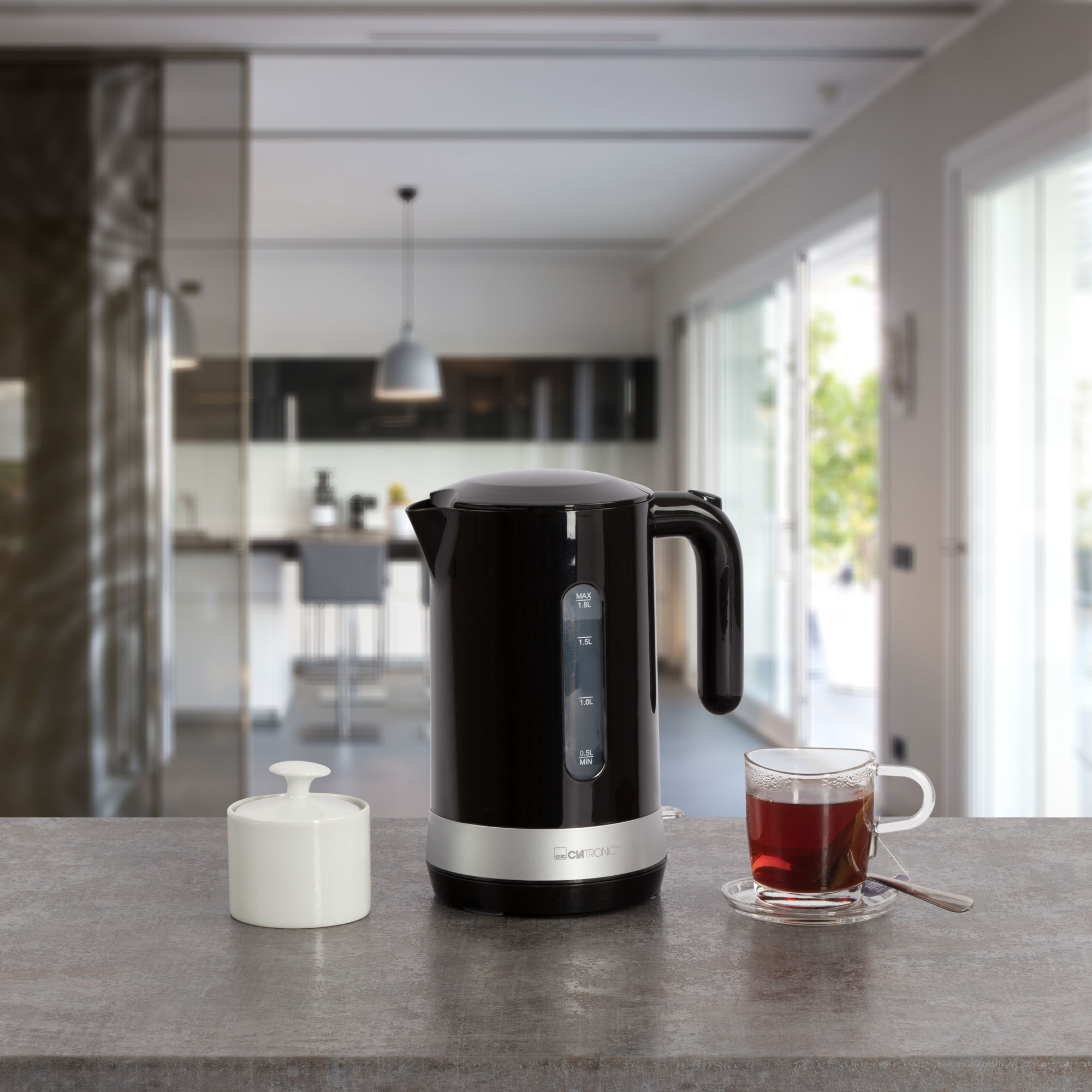 Schwarzer Wasserkocher und eine Teetasse mit Tee auf einer Küchenarbeitsplatte. Verschwommener Hintergrund.
