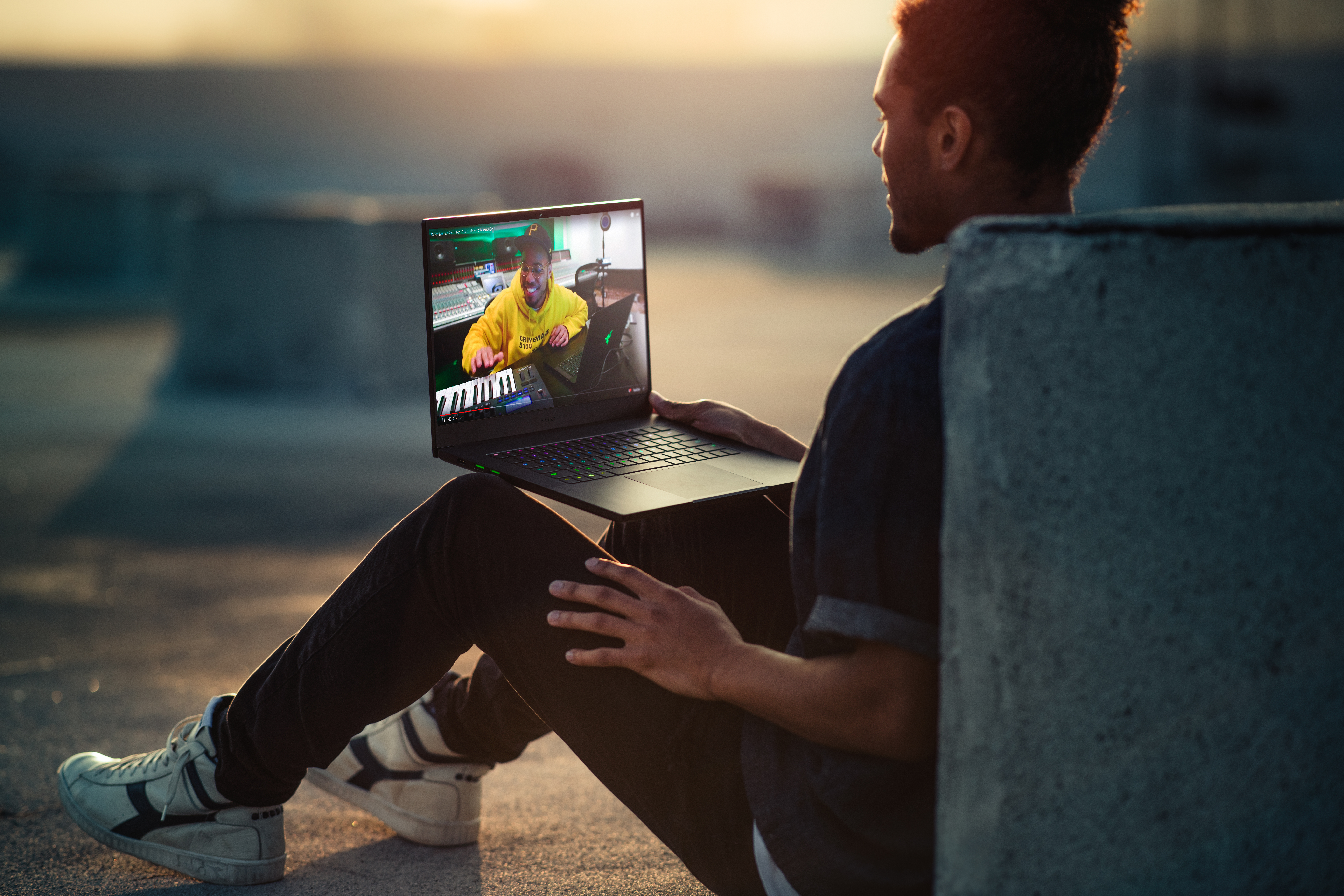 Ein Mann sitzt auf einem Dach und schaut auf einen Laptop-Bildschirm, der ein Video zeigt.