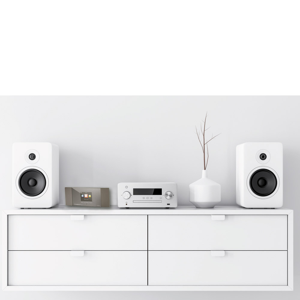 Ein weißes Sideboard mit zwei Lautsprechern und Audiogeräten. Eine Vase mit Zweig steht oben.
