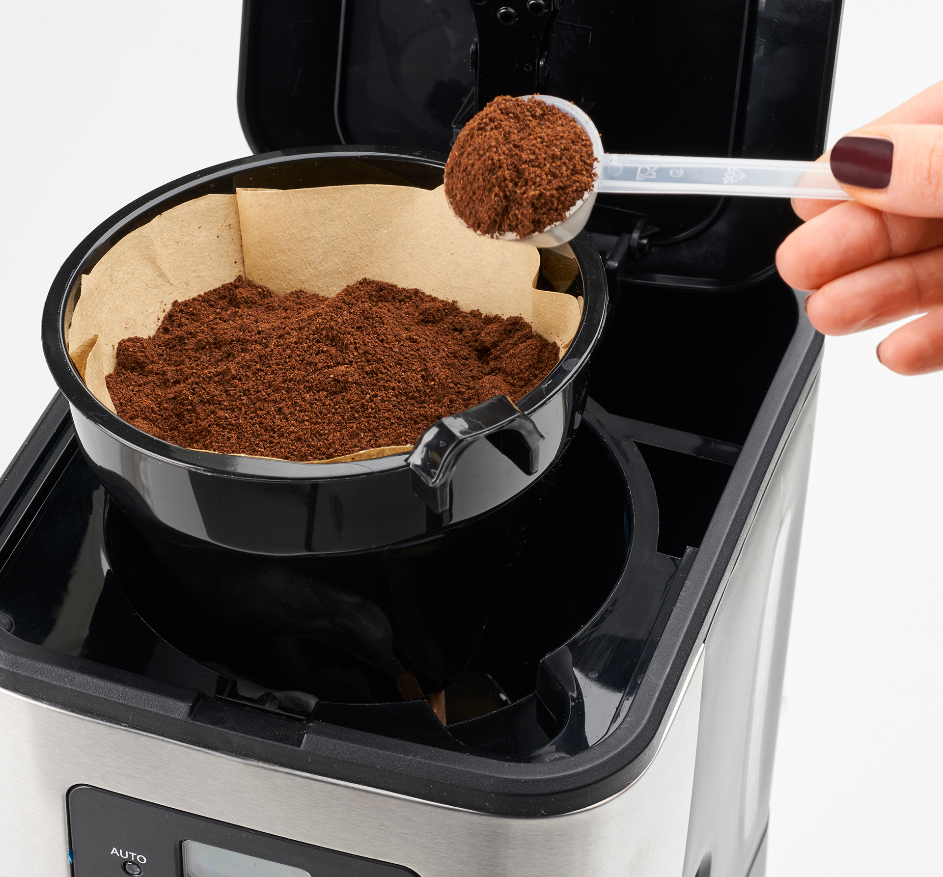 Kaffeemaschine mit Filter, der mit Kaffeepulver gefüllt wird, mit einem Löffel.