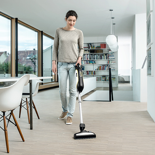 Eine Frau saugt einen Holzboden in einem modernen, hellen Haus mit einem schwarz-gelben Staubsauger.