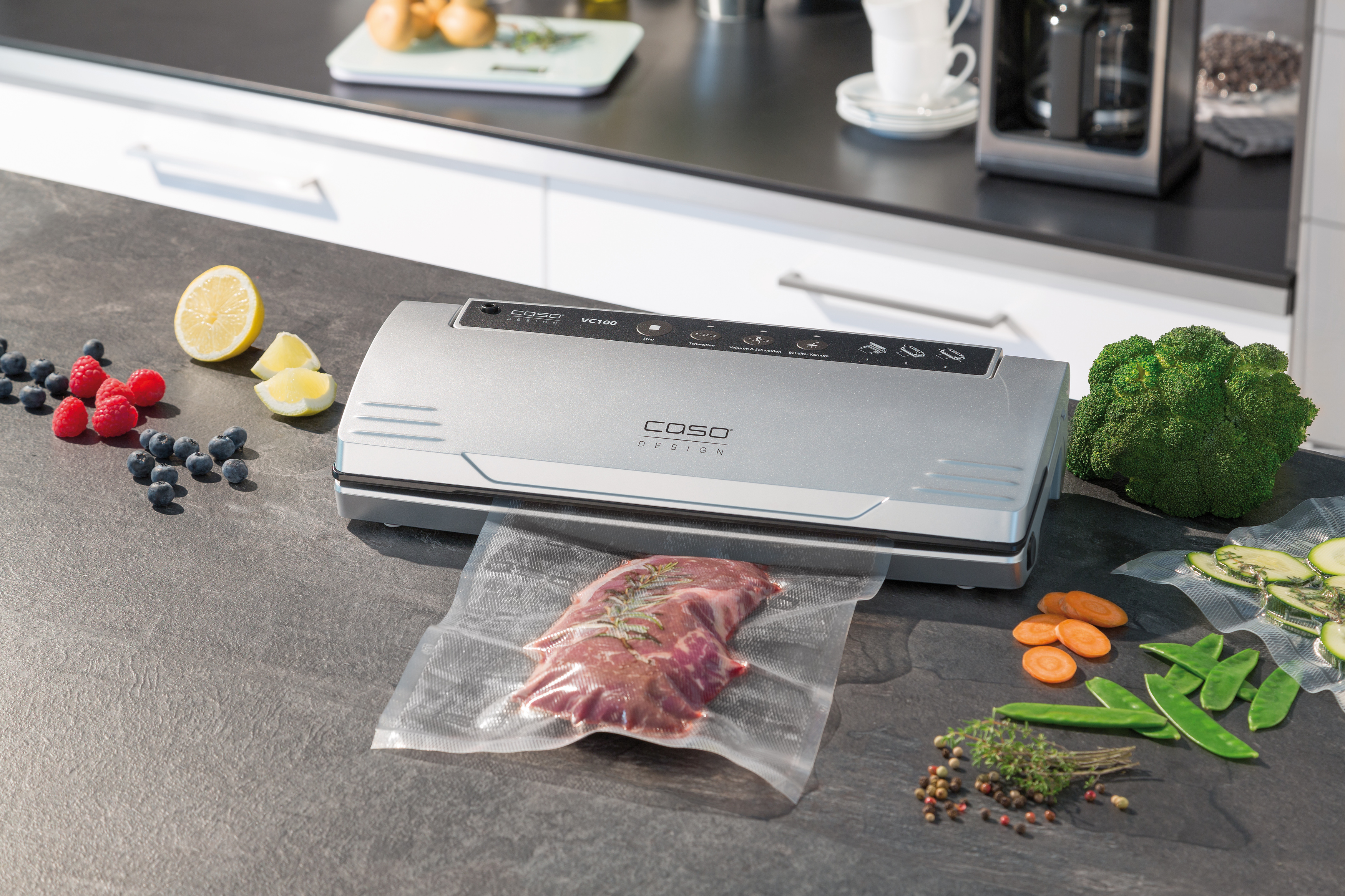 Silberner Vakuumierer mit Lebensmitteln, darunter Fleisch und Gemüse, auf dunkler Oberfläche.