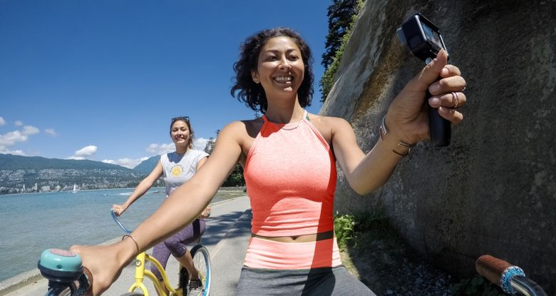 Twee vrouwen fietsen op een zonnige dag. Eén houdt een camera vast.