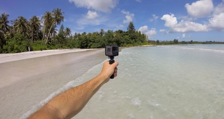 Een persoon die een GoPro-camera op een stok vasthoudt en een strandscène met helder water vastlegt.