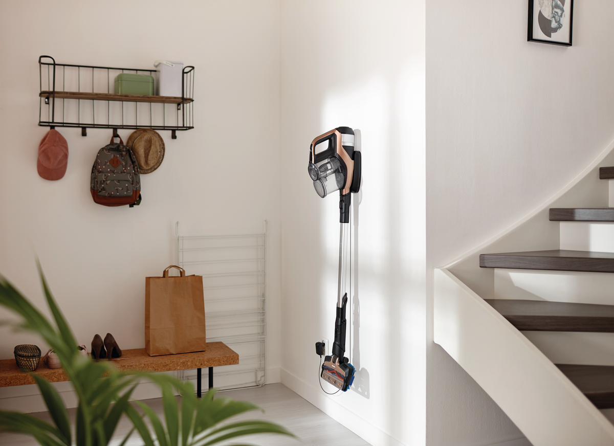 Weiße Wand mit Staubsauger. Schuhe, Tasche und Treppe sind in der Szene zu sehen.