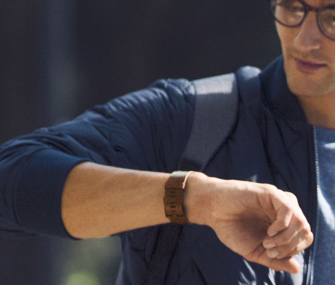 Un homme portant une montre à son poignet et une veste bleue. Il regarde sa montre.