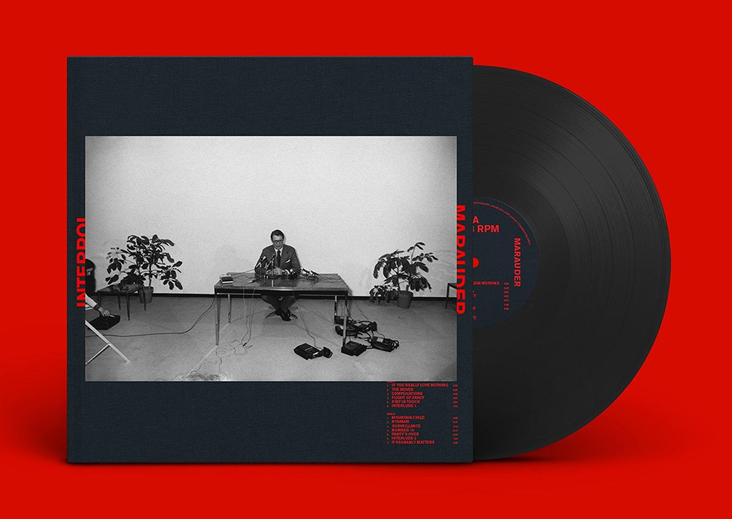Albumcover mit einem Mann an einem Tisch und einer Schallplatte auf rotem Hintergrund.