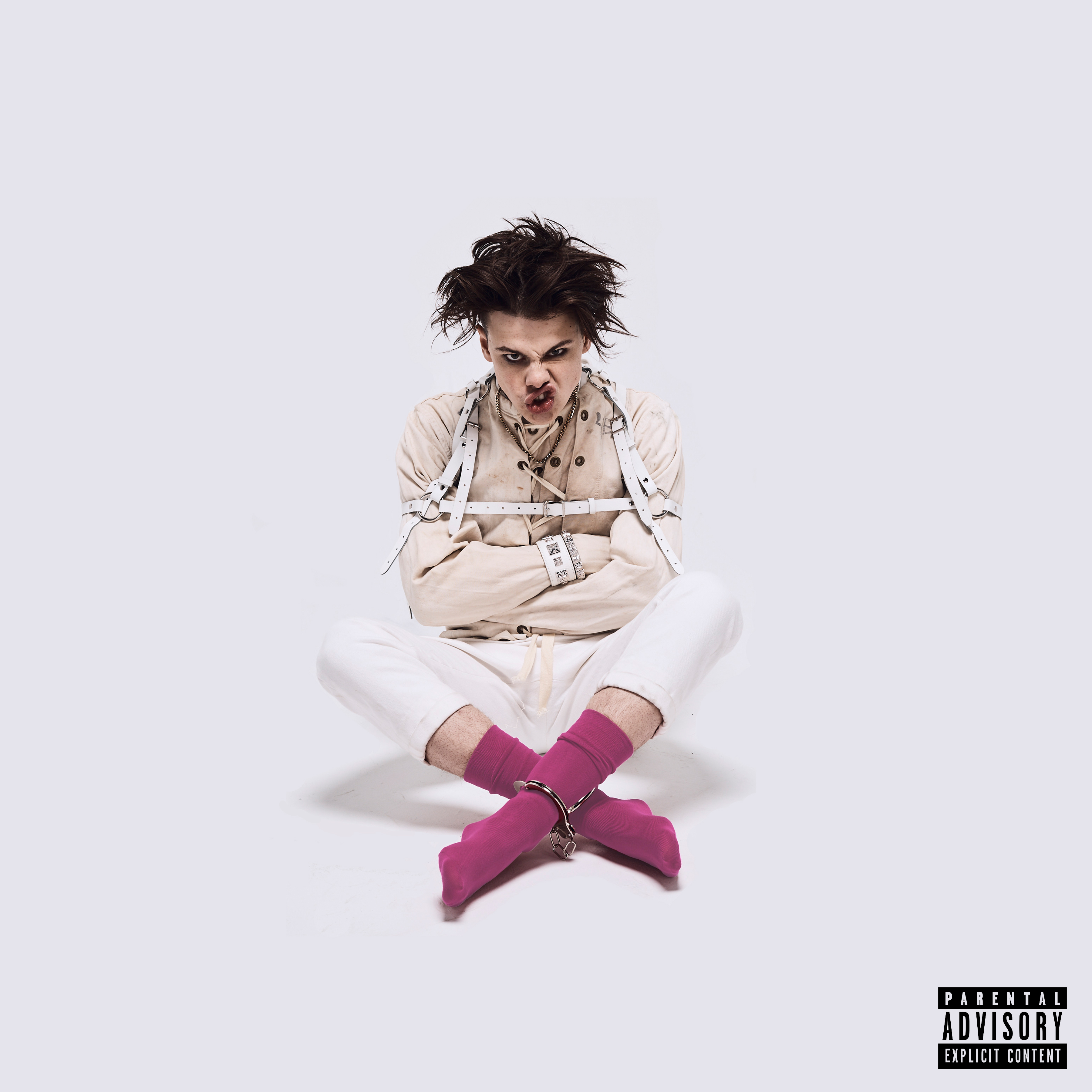 Mann in Fesseln, rosa Socken, sitzend. Einfacher Hintergrund. Schwarzes und weißes Parental Advisory Label.