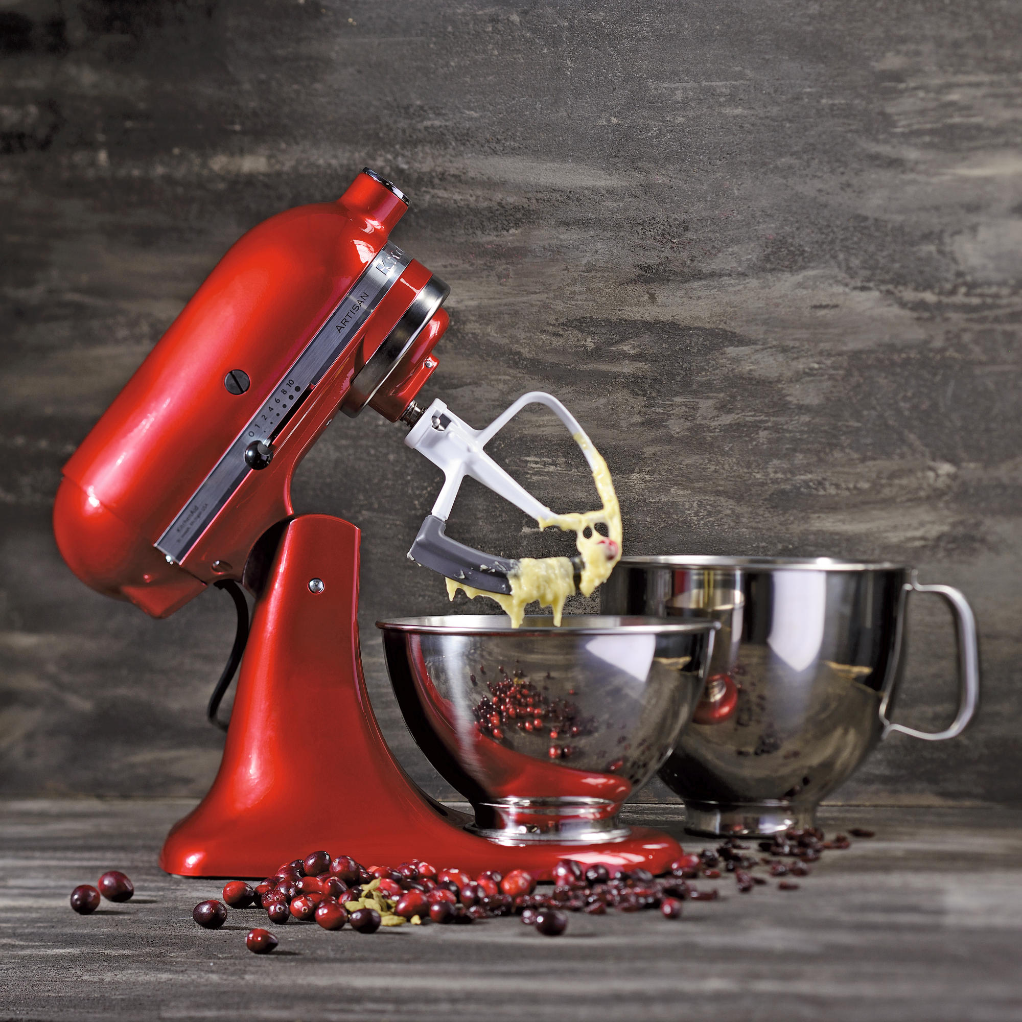 Roter KitchenAid-Küchenmixer mit Aufsätzen und Schüsseln. Preiselbeeren auf dem Tisch. Grauer Hintergrund.