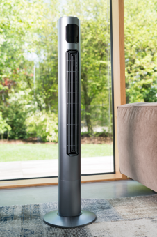 Hoher, silberner, zylindrischer Turmventilator vor einem Fenster.