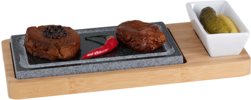 Zwei Fleischportionen auf einem Steinplatte mit roter Paprika und eingelegten Gurken in einer Schüssel.