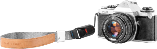 Appareil photo vintage avec une sangle en cuir et une dragonne, sur fond noir. L'appareil est argenté.